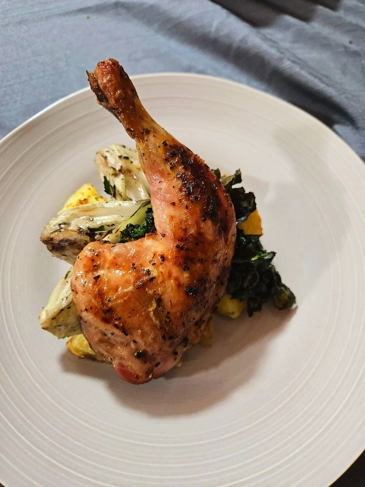 Grilled chicken leg on a white plate with roasted vegetables underneath.