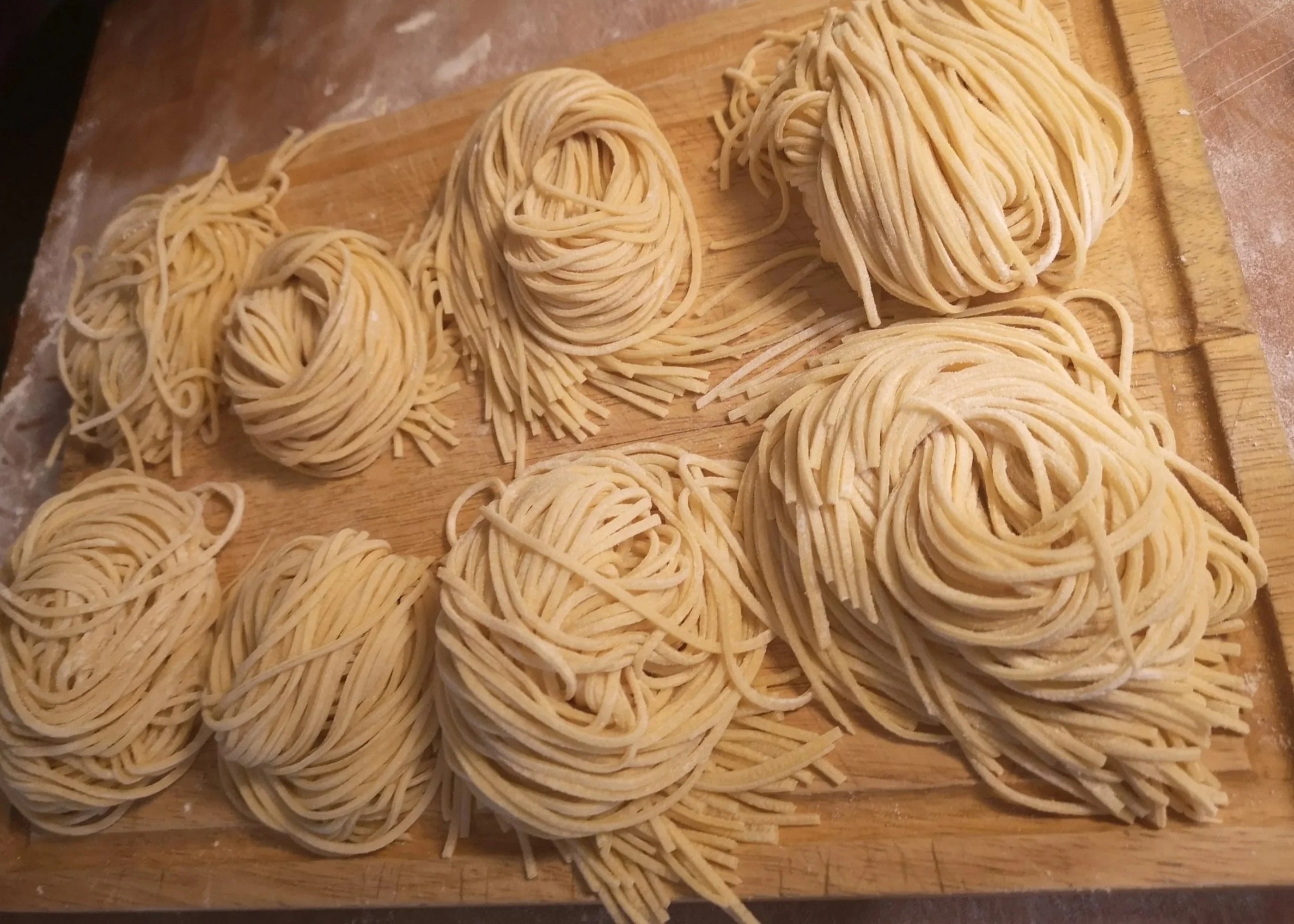 Uncooked pasta nests on a wooden cutting board, with some strands scattered around.