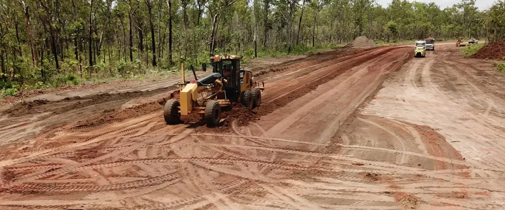 Construction vehicles working on a dirt road construction site in a wooded area.
