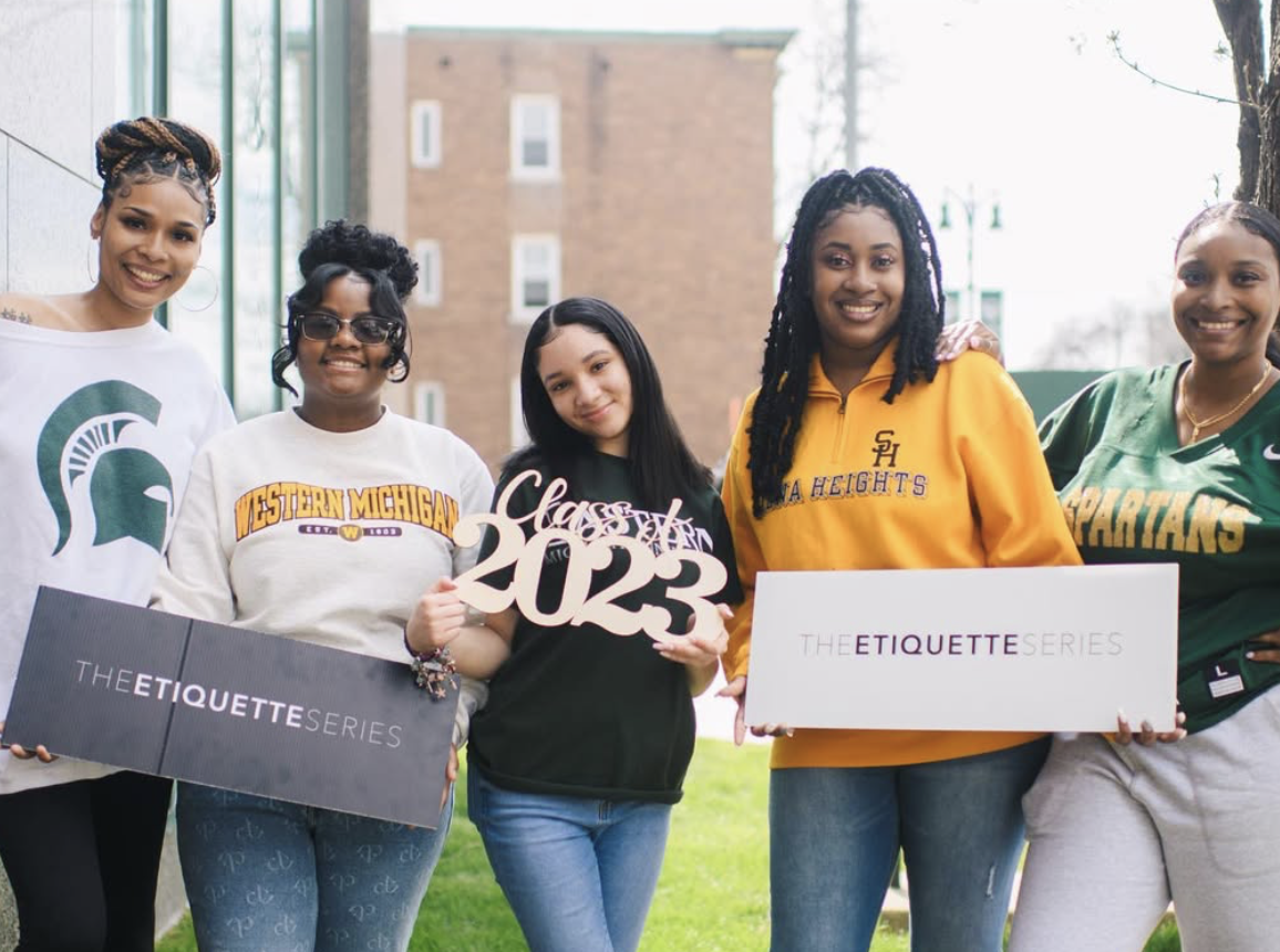 Group of five young women standing outdoors, smiling, holding signs that read 'The Etiquette Series,' and a 'Class of 2023' sign, with a building in the background. The Etiquette Series, Chicago-Detroit.