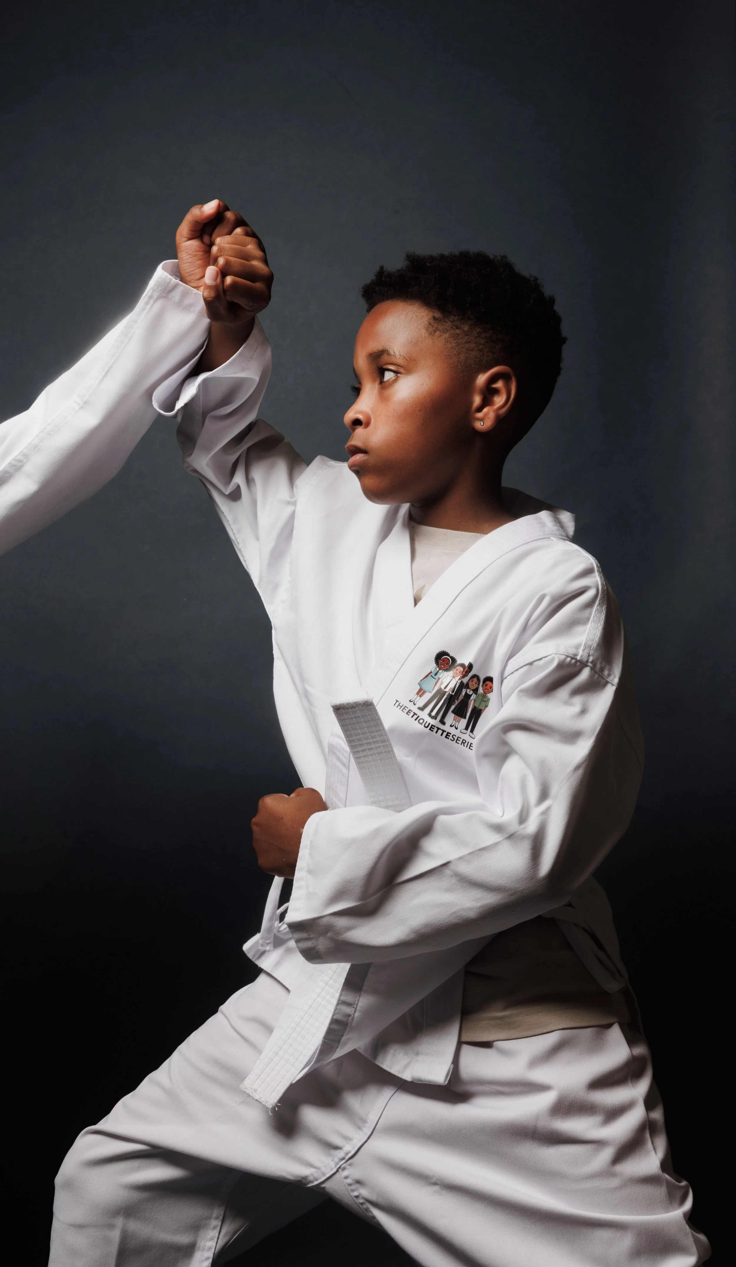 A young person practicing martial arts in a white uniform with a white belt, demonstrating a technique against a dark background.