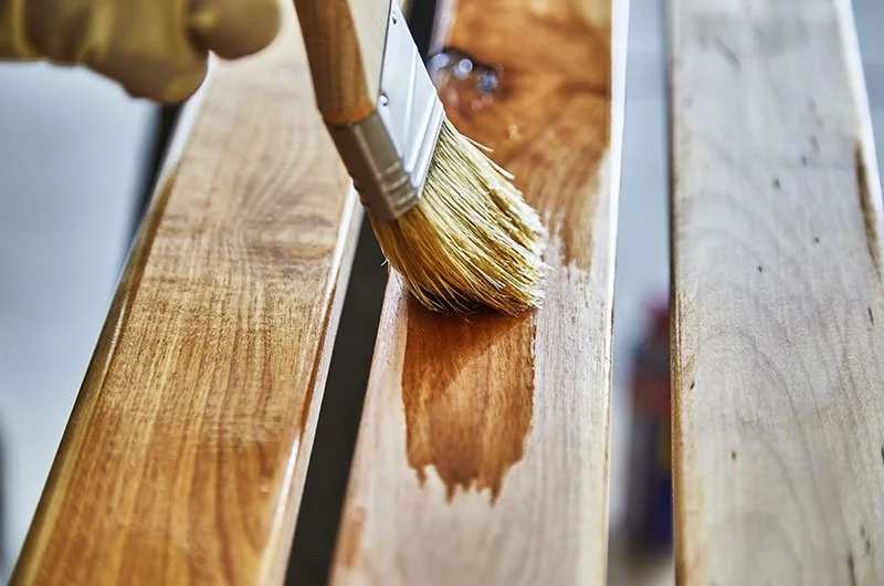 A woodworker applying a premium clear varnish to seal a bespoke natural timber surface