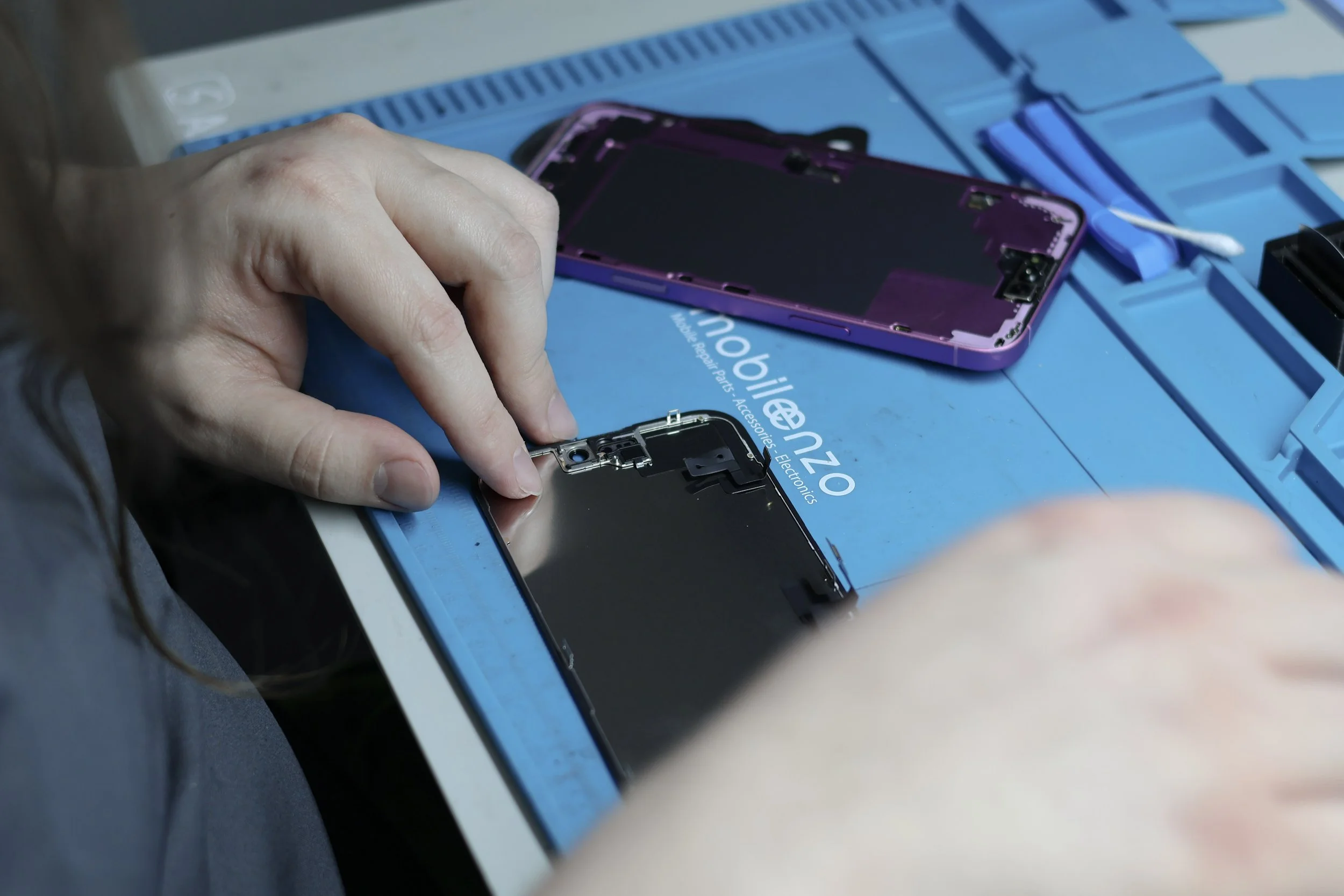 A technician assembling a smartphone with a disassembled purple phone on the table.
