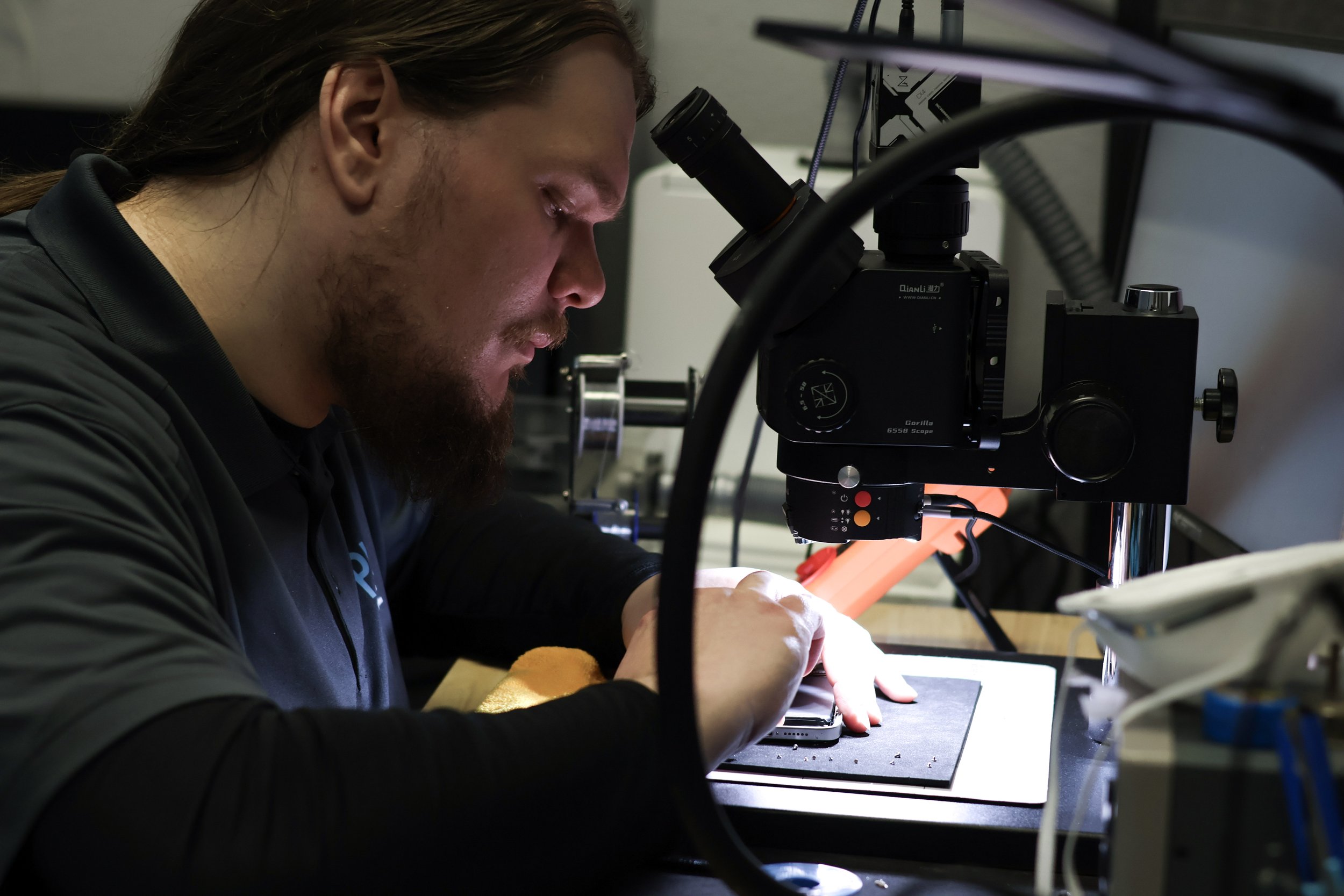 A man working in a laboratory using a microscope to examine a small object, with a bright light illuminating his workspace.