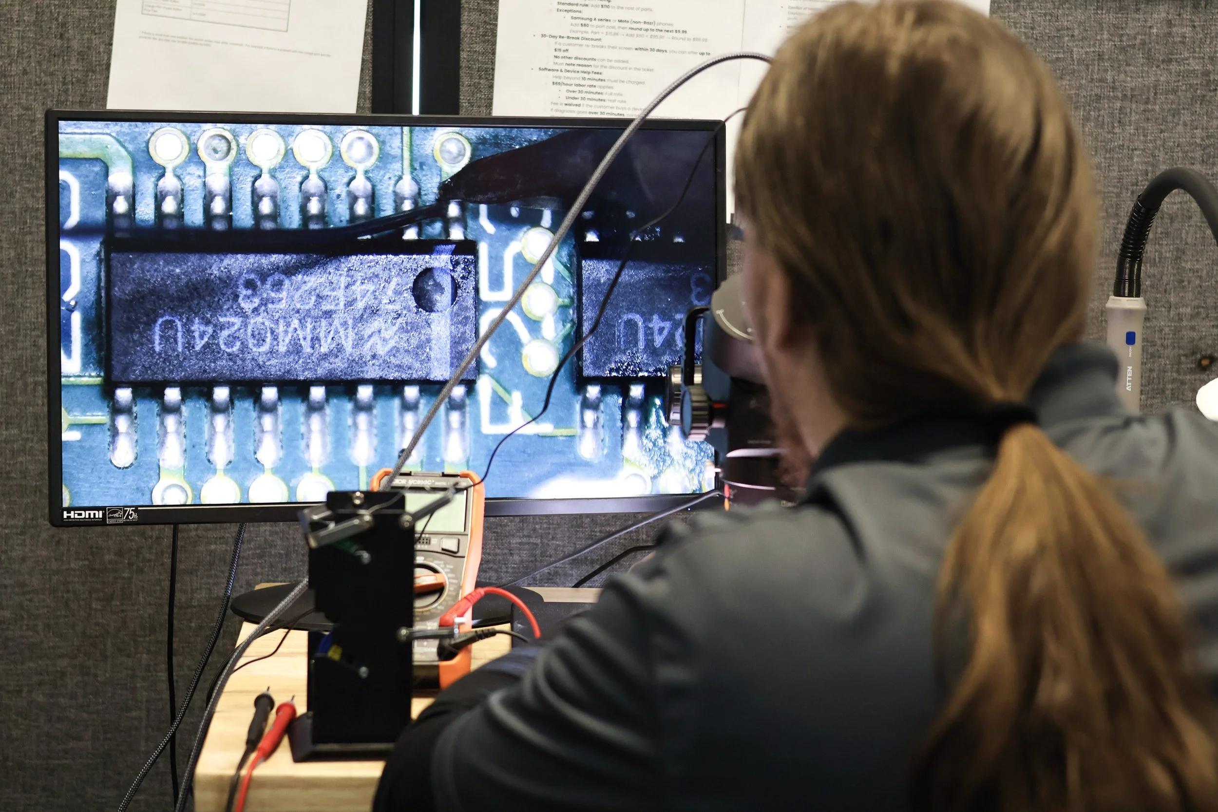 Person working on a technical project with electronic components on a computer monitor, connected to testing equipment, in a lab setting.