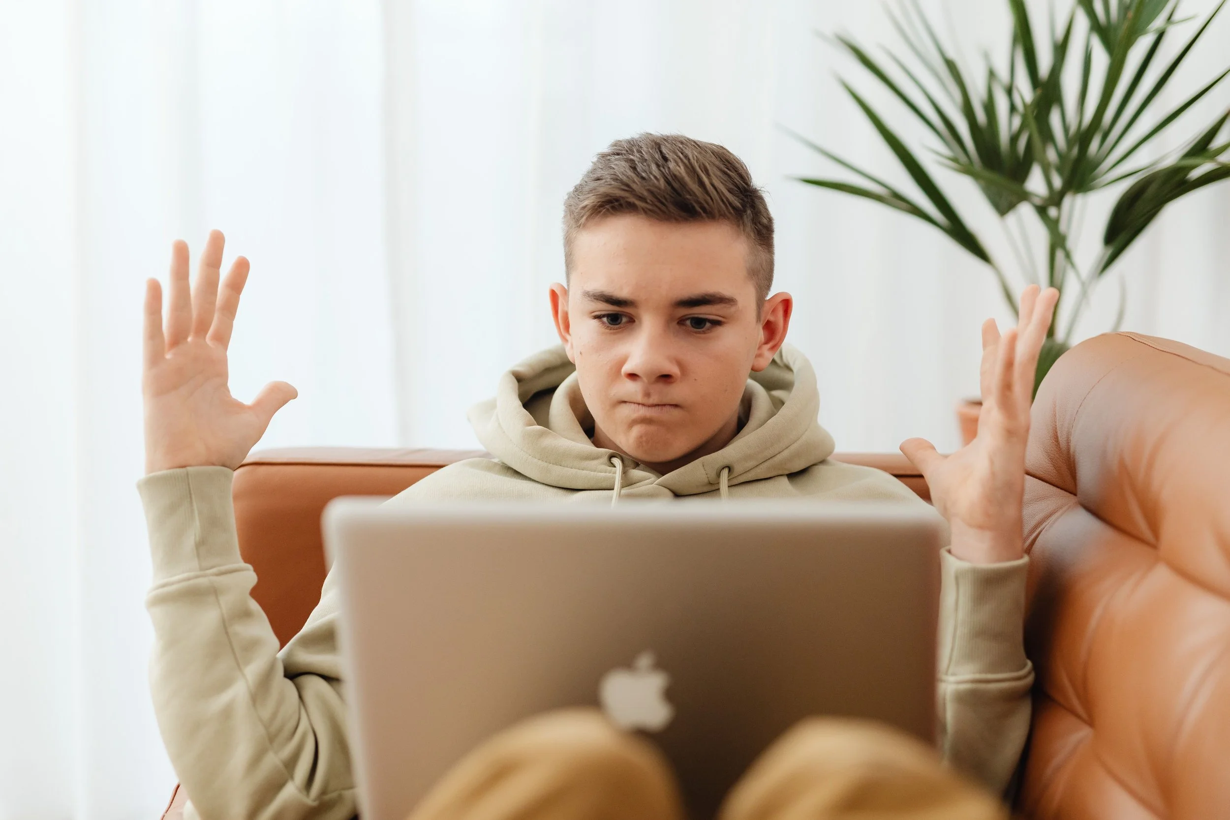 Teenager looking frustrated while dealing with data loss on a MacBook.