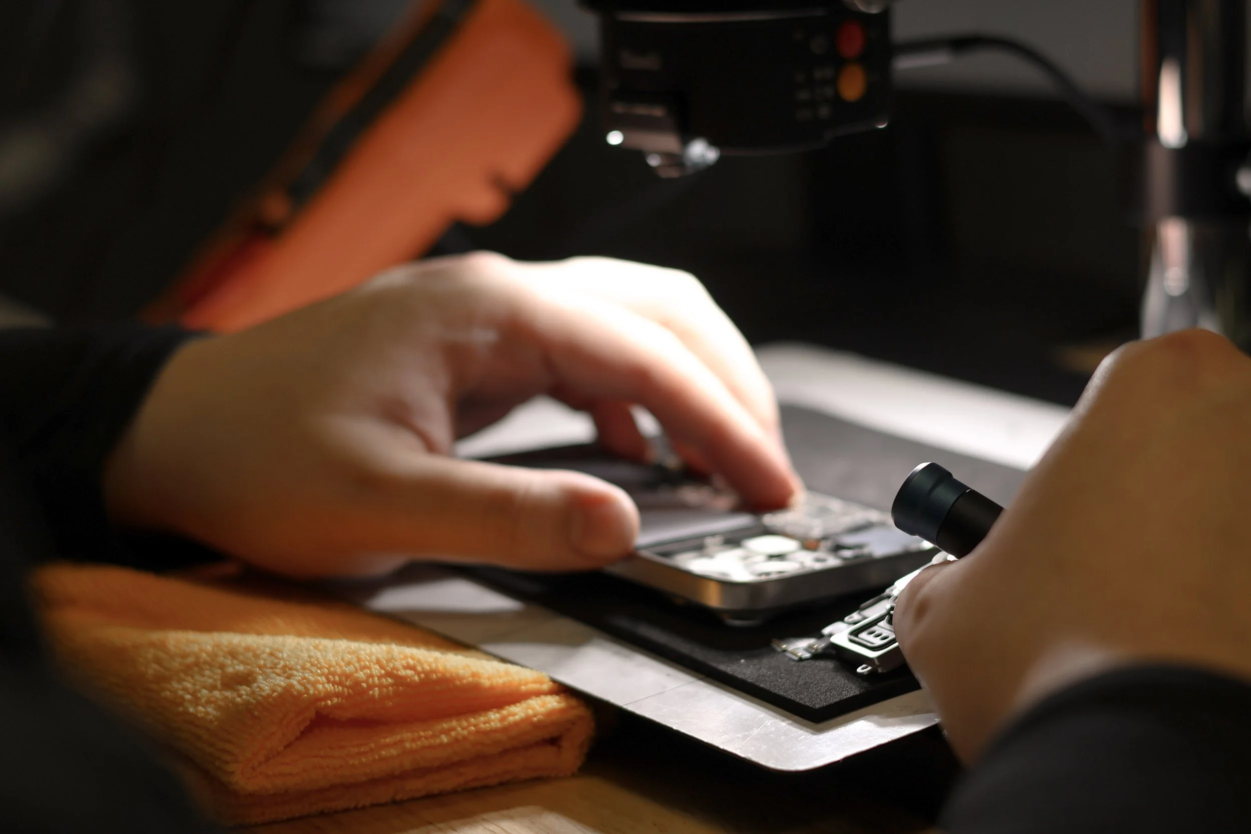 Person examining an electronic device under a microscope in a laboratory.
