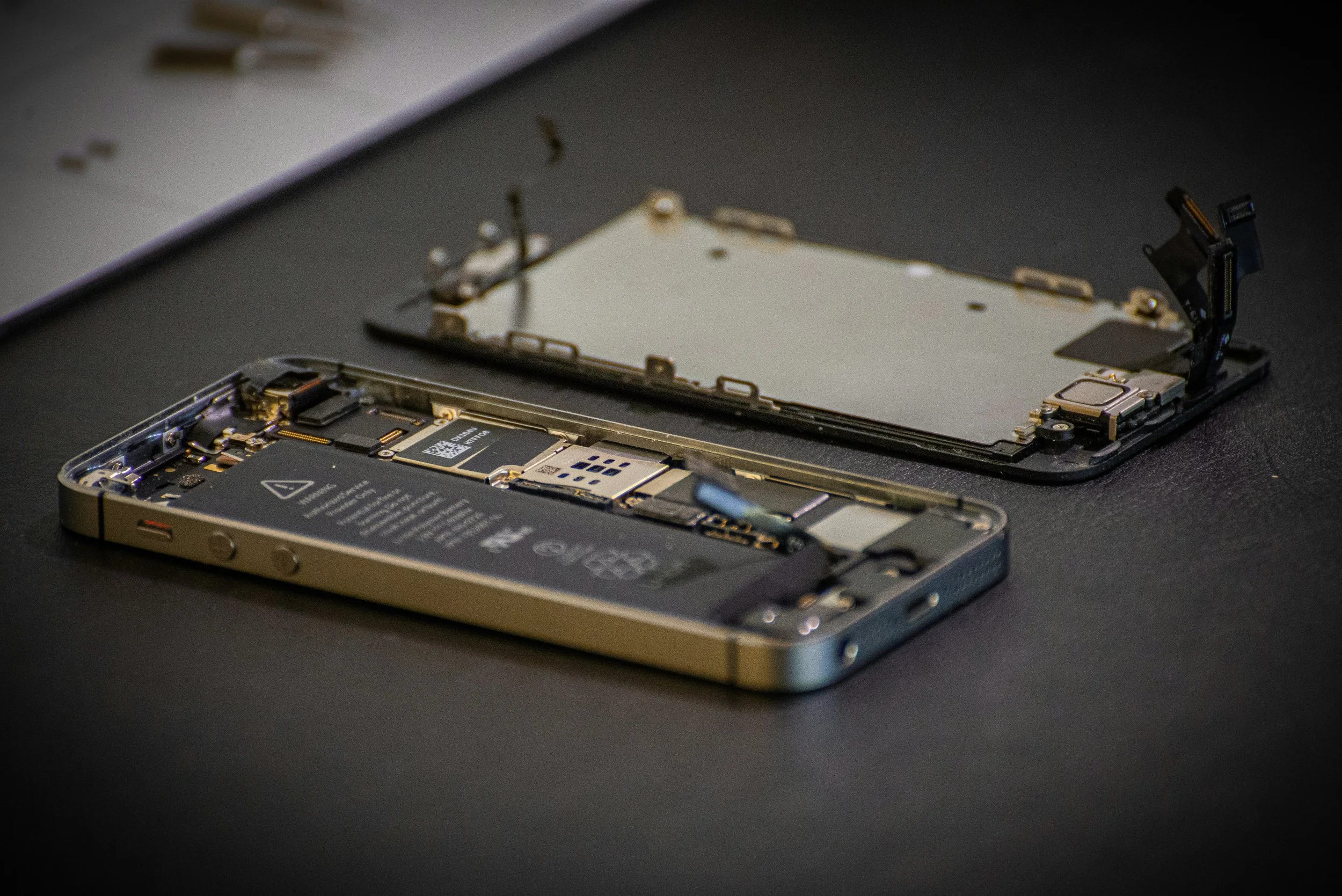 Disassembled smartphone on a repair mat with internal components exposed.