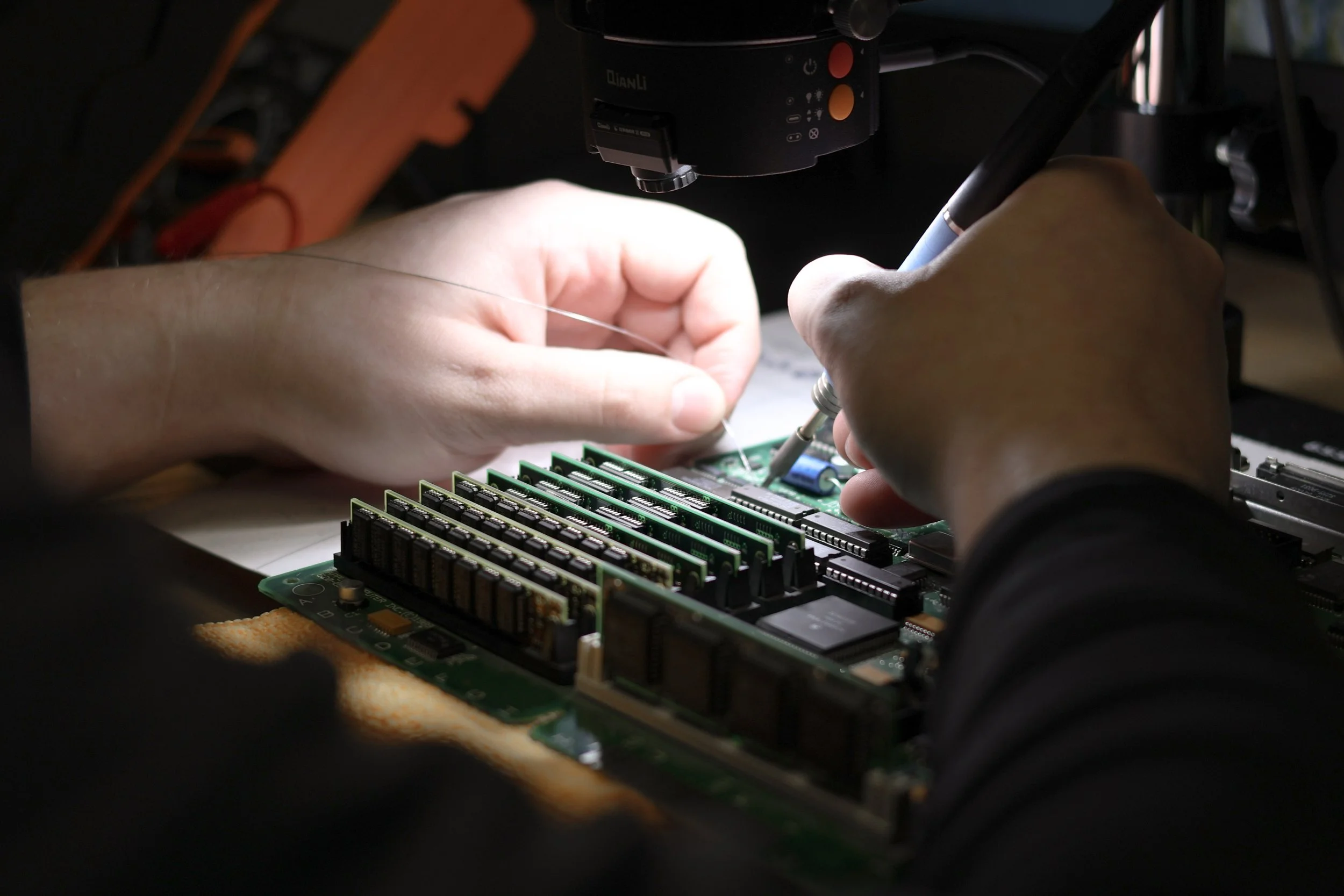 Person repairing a computer motherboard with a soldering iron.
