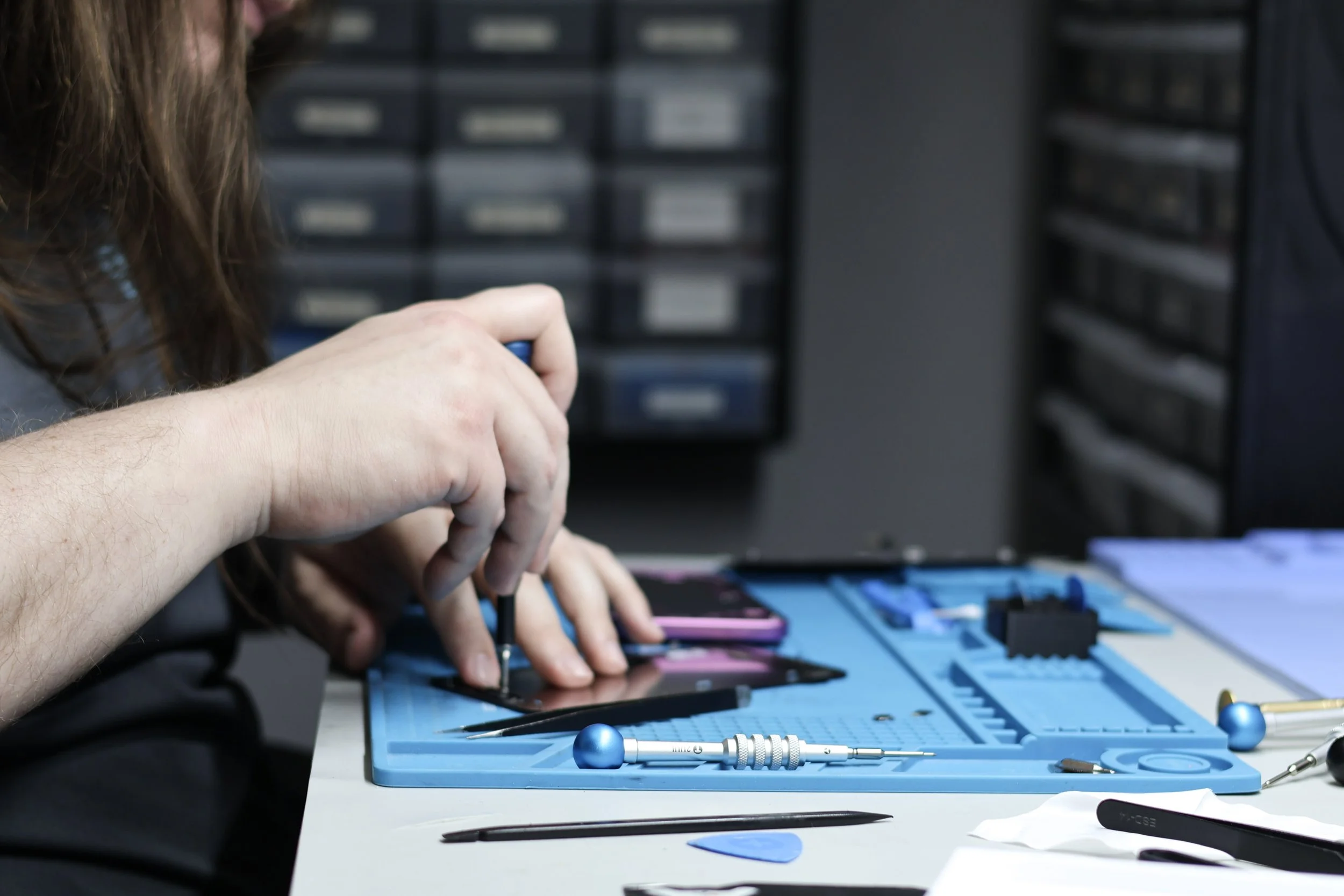 Person assembling a smartphone at a workbench with tools and electronic components.