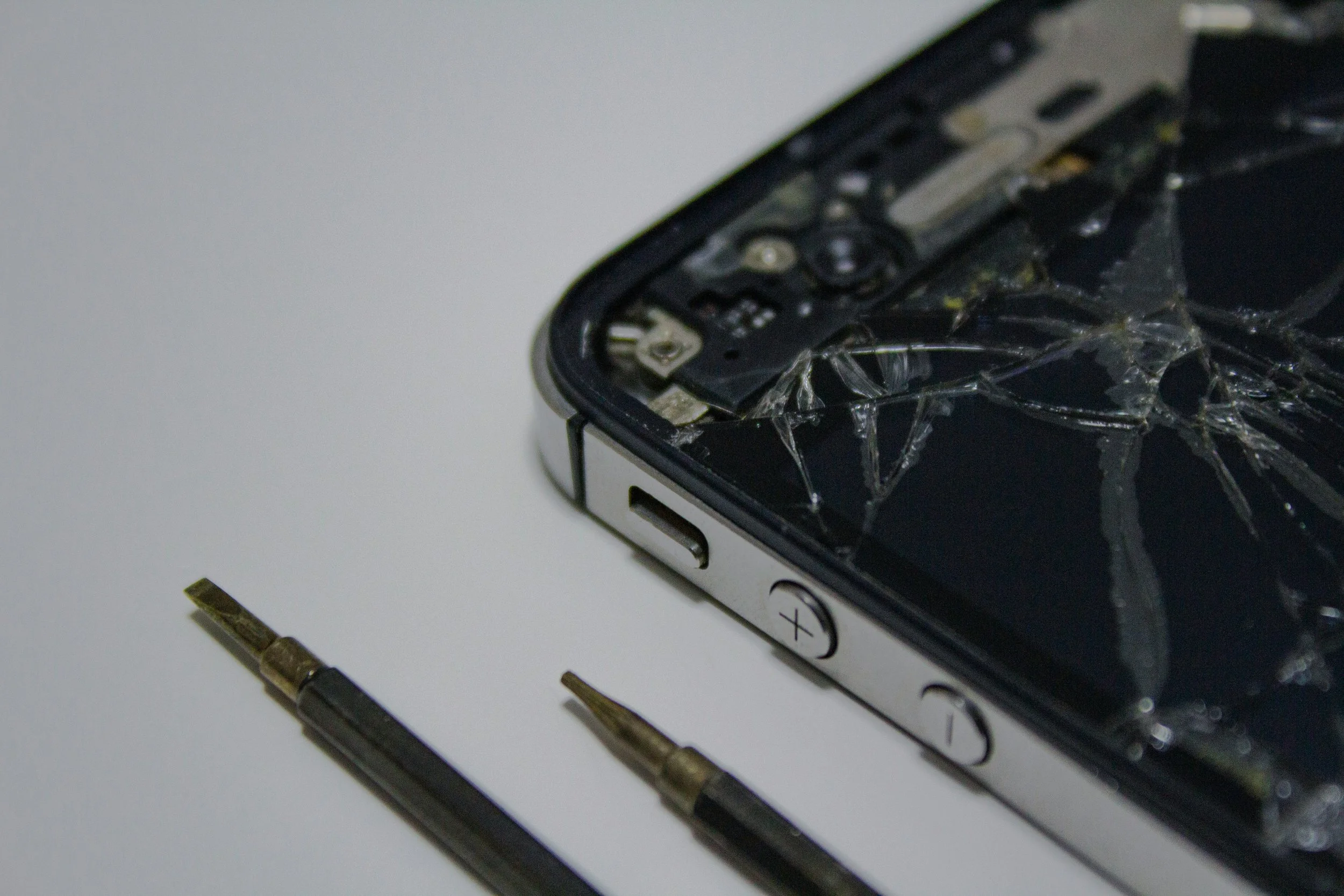 Close-up of a cracked phone screen with repair tools on the side