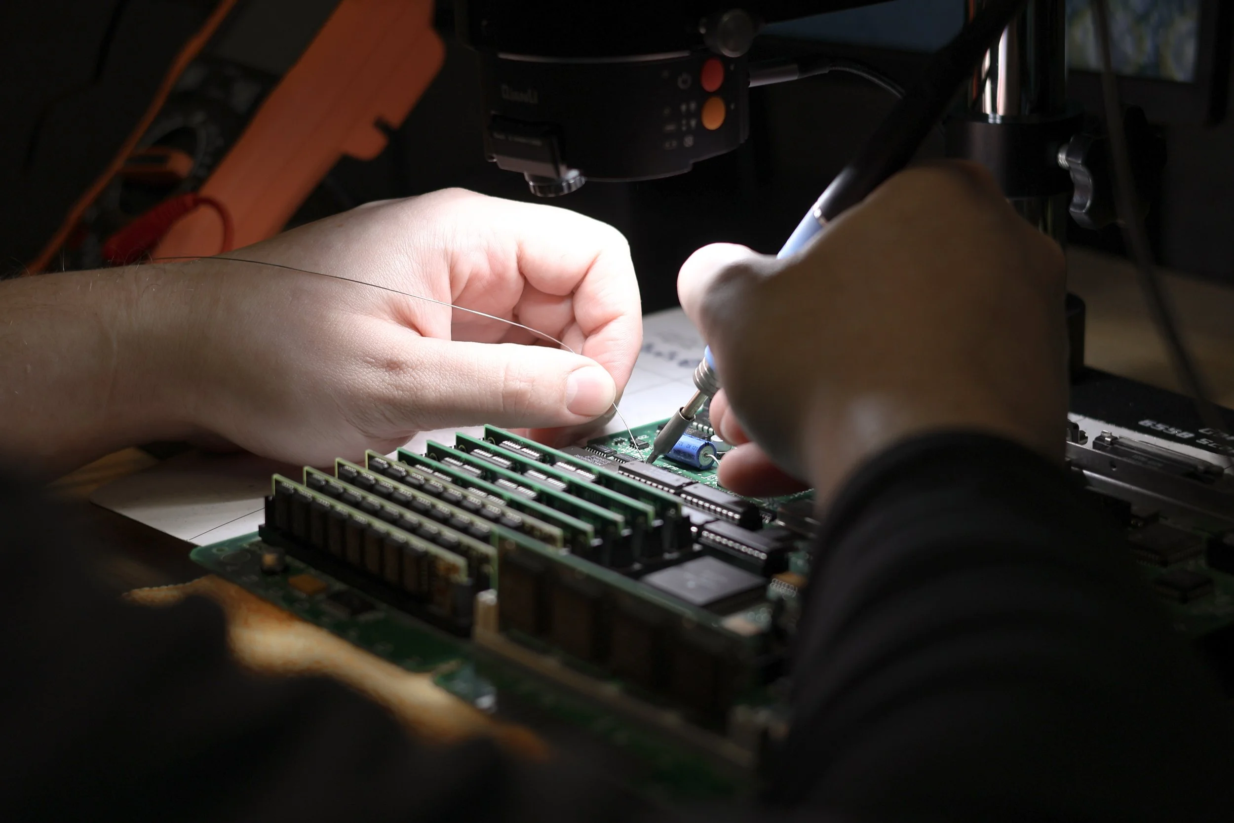 A person repairing a computer motherboard with a screwdriver in a dark room.