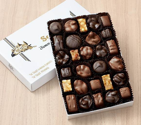 Open box of assorted chocolates on a light wooden surface.