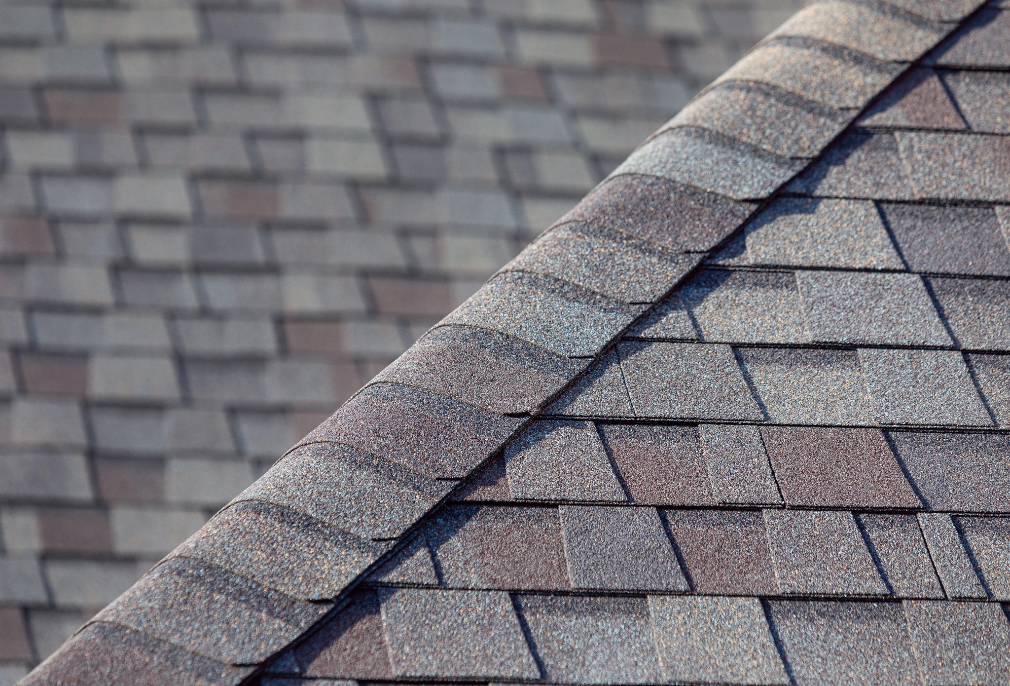 Close-up of a shingled roof, showing two different sections with asphalt shingles in shades of gray and brown.
