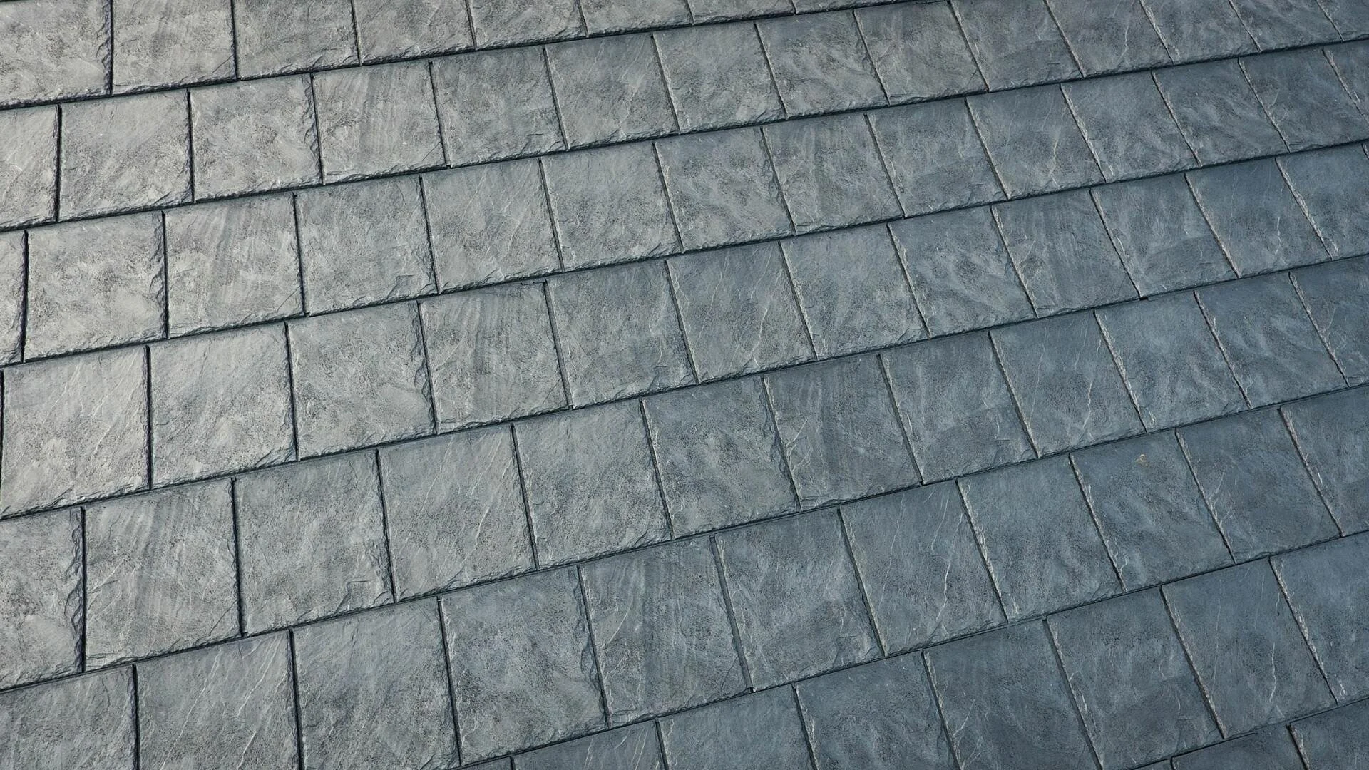 Close-up of a roof with gray, rectangular shingles arranged in a pattern.