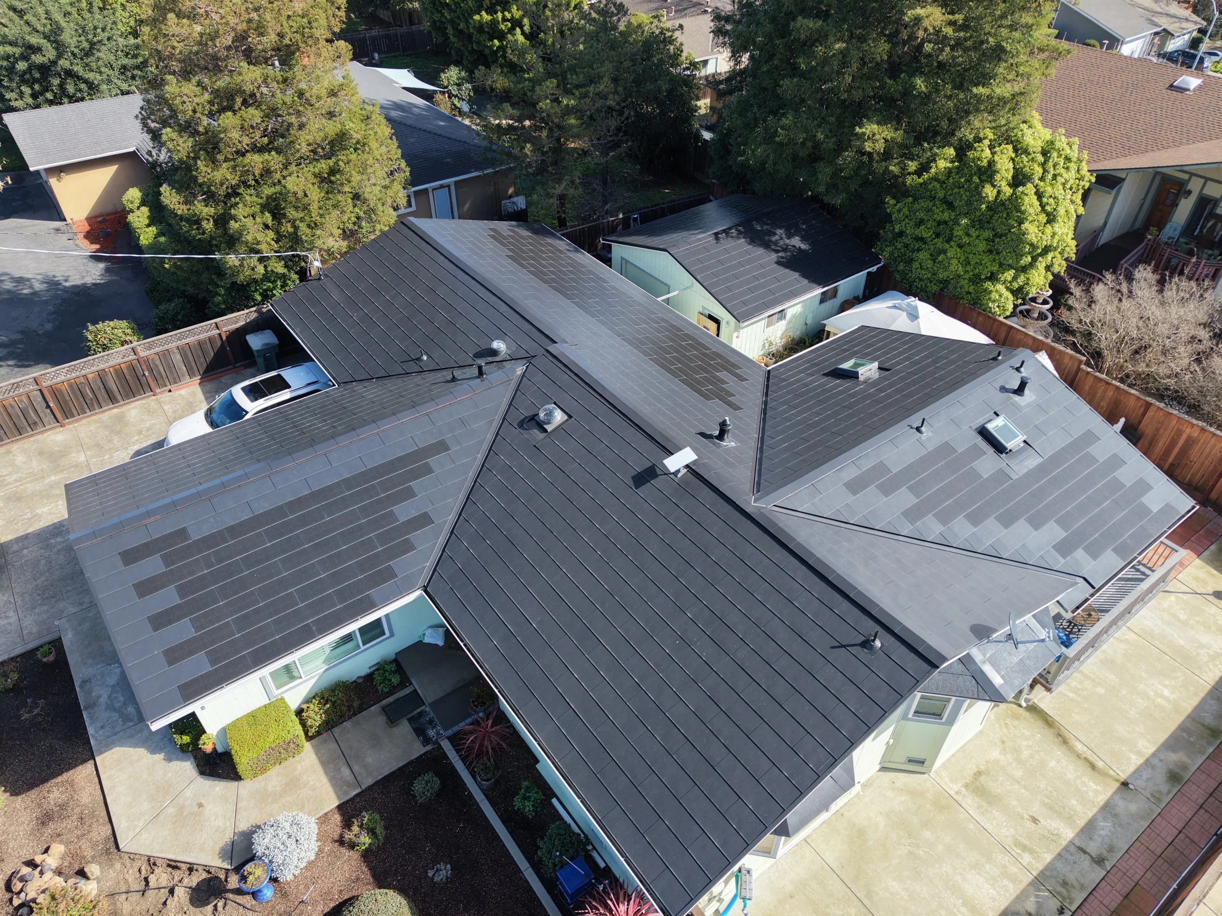 An aerial view of a residential neighborhood showing rooftops, trees, and a backyard with plants and garden decorations.