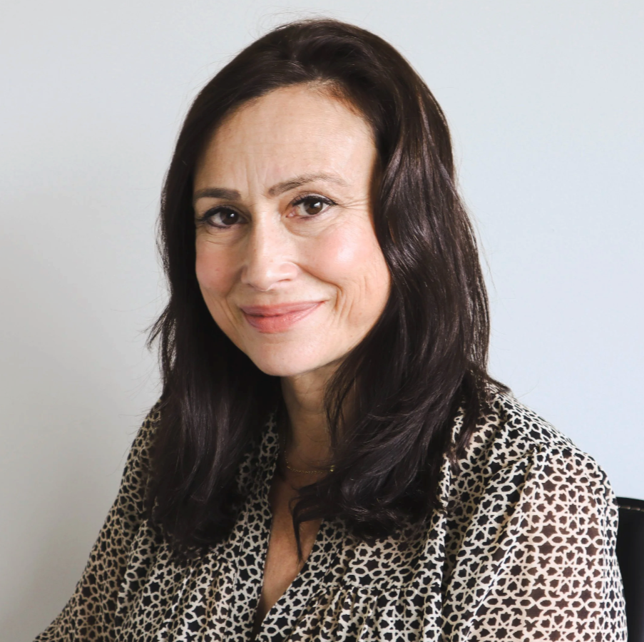 Portrait of a woman with dark brown hair wearing a leopard print top, smiling softly at the camera against a plain white background.