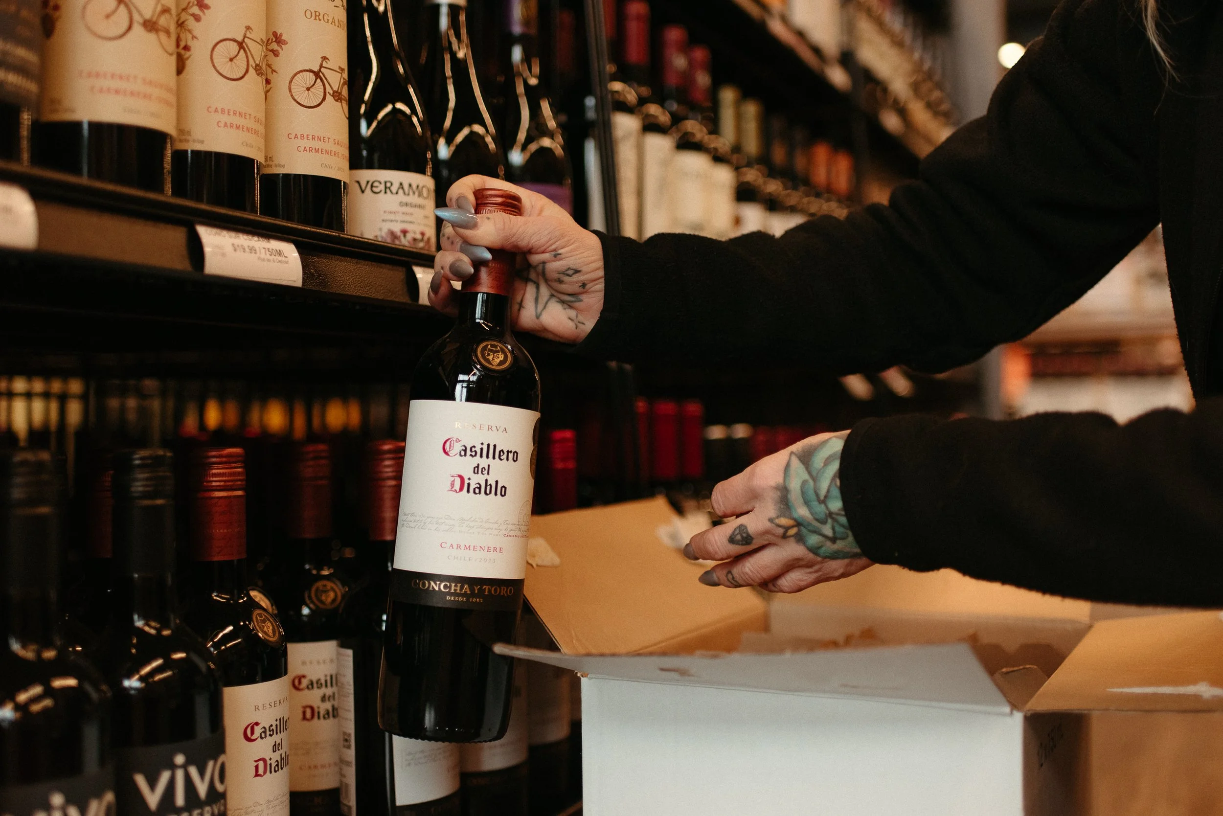JAK's Beer Wine Spirits staff member selecting a bottle of Casillero del Diablo from the wine shelf