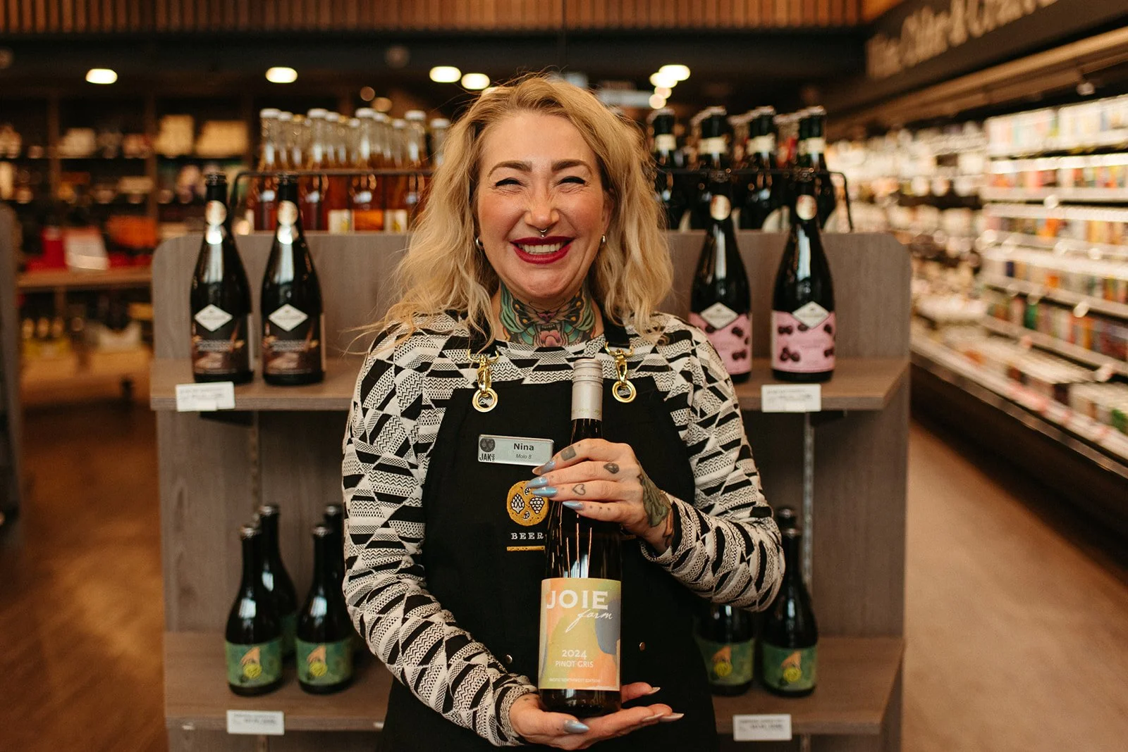 JAK's Beer Wine Spirits staff member Nina smiling and holding a bottle of Joie Farm Pinot Gris in store