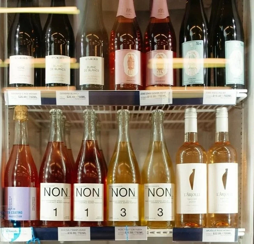 Display of various bottles of wine and rosé wine on a grocery store refrigerator shelf.