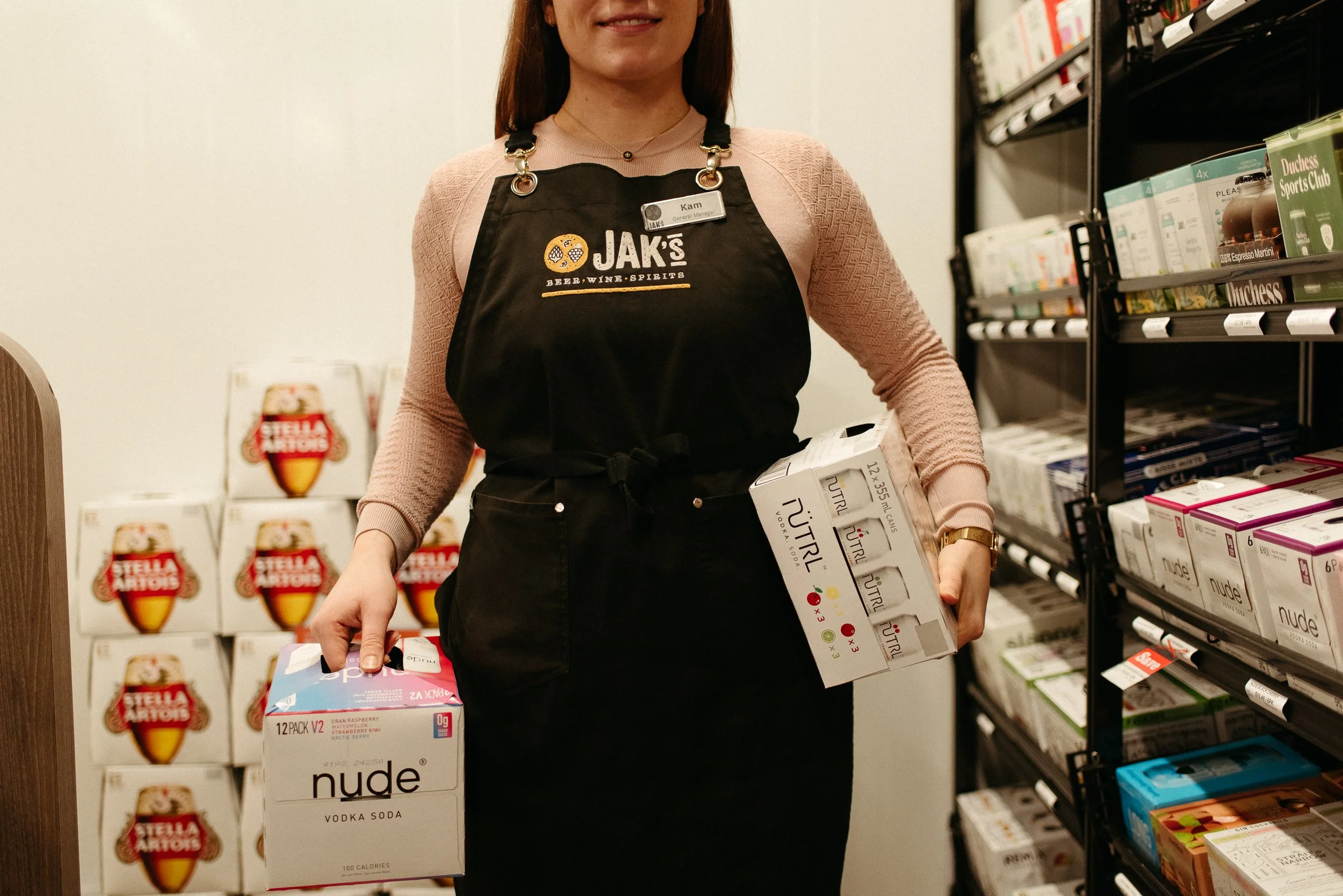 JAK's Beer Wine Spirits staff member in apron holding Nude and NUTRL ready-to-drink products in store