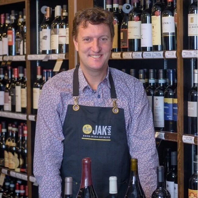 Mike McKee, (John's Son-in-law) Shareholder at JAK's Beer Wine Spirits, standing in front of a wine shelf in a JAK's store in Vancouver.