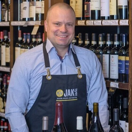Tim Dumas, (John's nephew)  Shareholder at JAK's Beer Wine Spirits, standing in front of a wine shelf in a JAK's store in Vancouver