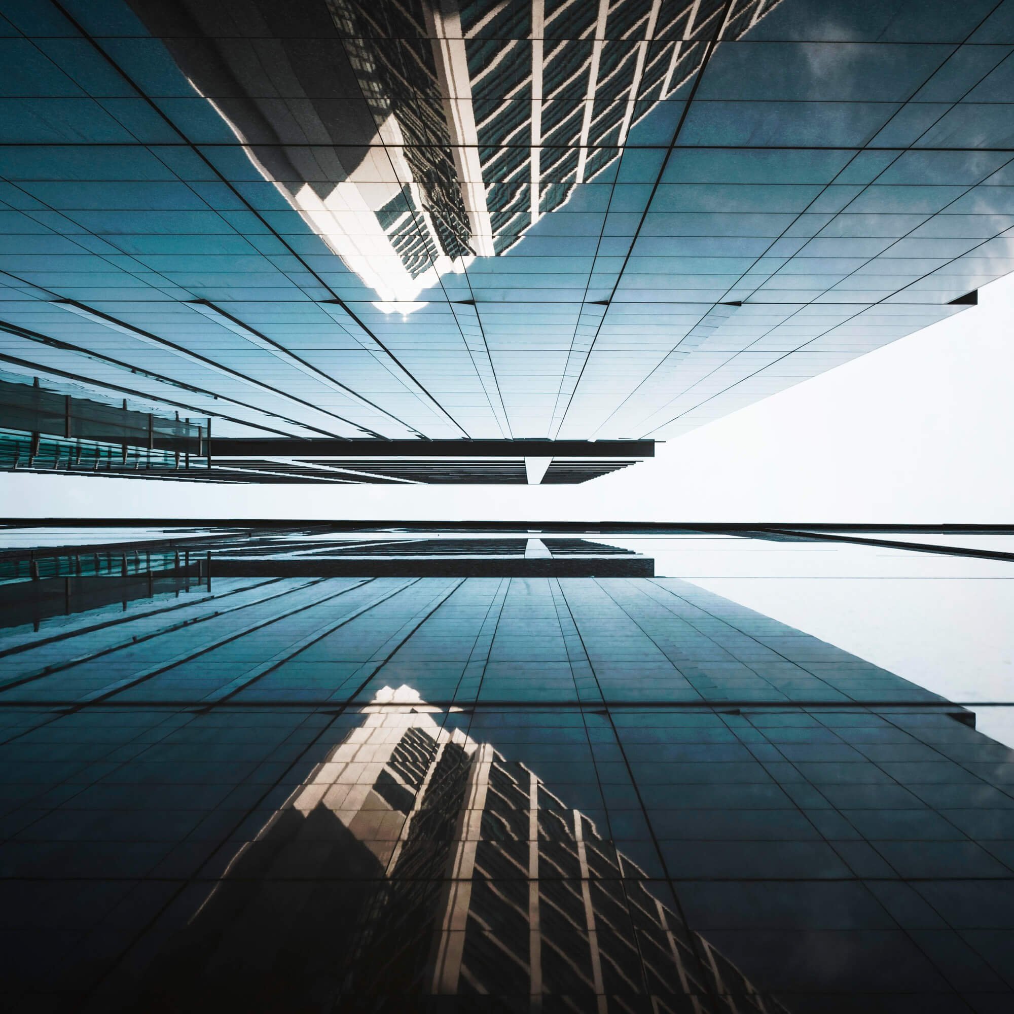 Looking up at tall glass skyscrapers with reflections, with a clear sky in the background.