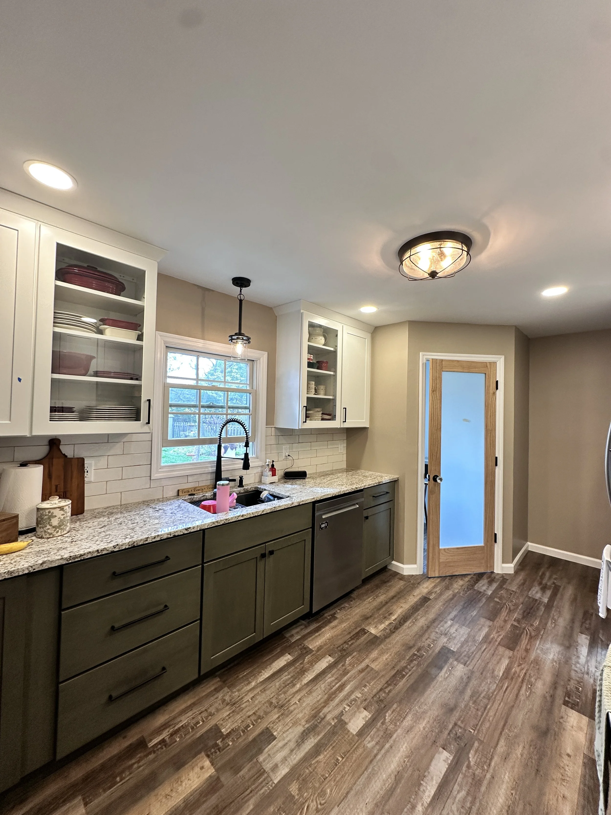 Kitchen with white upper cabinets with glass doors, green lower cabinets, granite countertops, a window above the sink, and wood-look flooring.