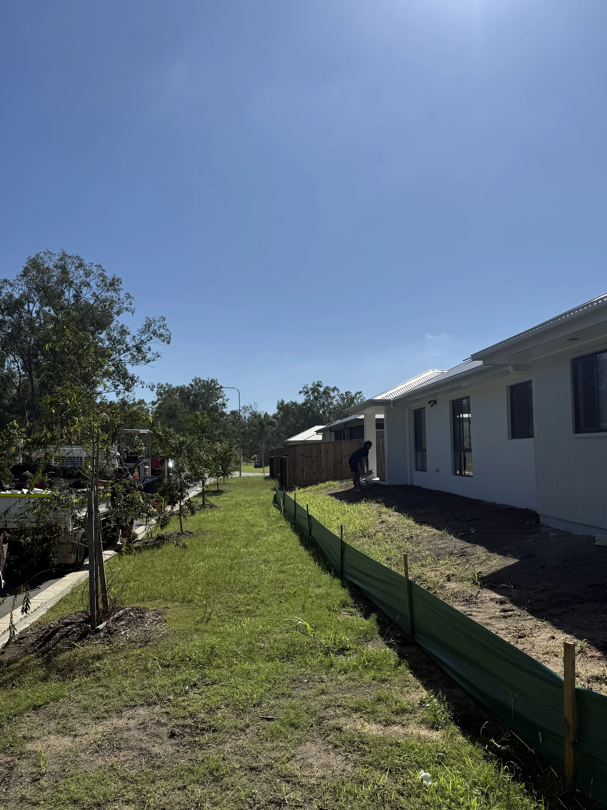 Person working on a garden next to a white house under a clear blue sky