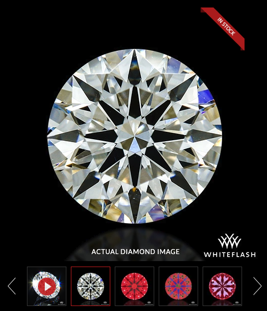 Close-up of a sparkling round diamond with a black background and a red "In Stock" label, featuring the White Flash logo.