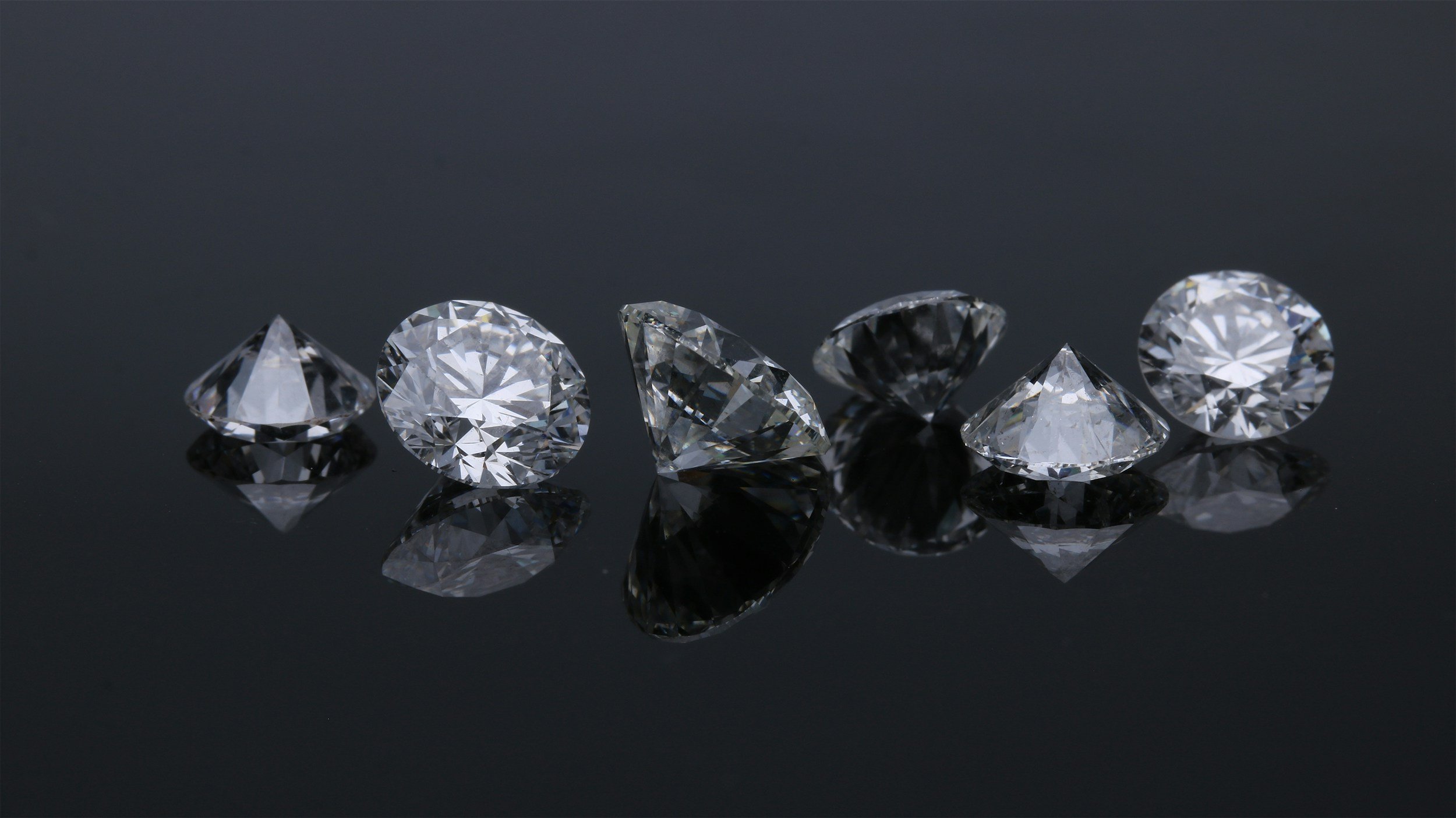 Six diamonds arranged in a row on a black reflective surface.