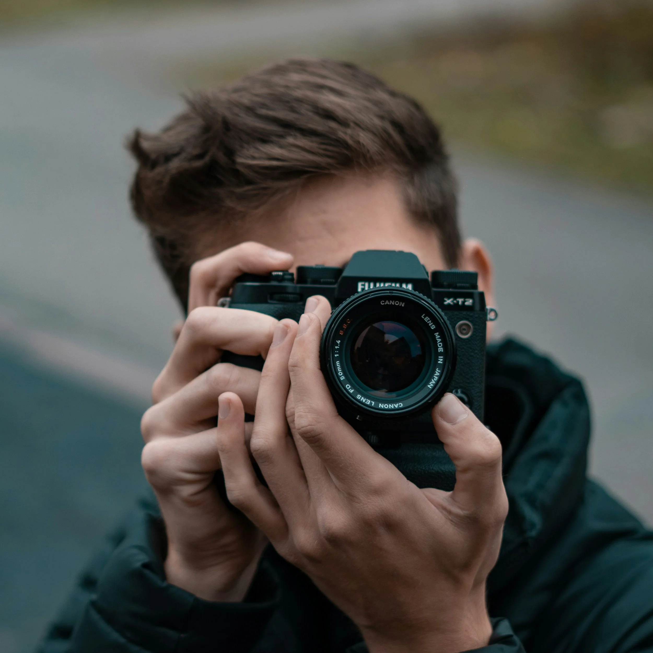Person holding a DSLR camera and taking a photo, focusing directly into the camera lens.