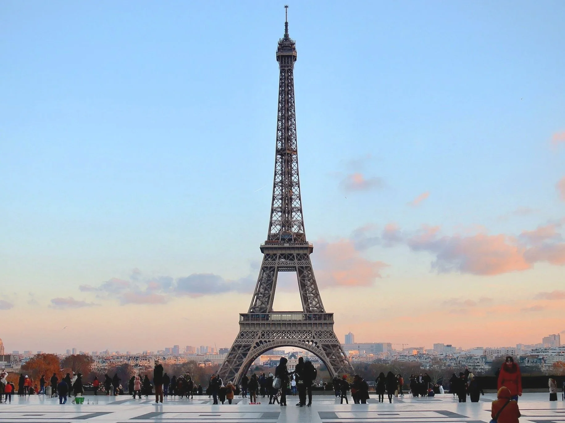 Eiffel Tower in Paris during sunset with people walking and taking photos in the foreground