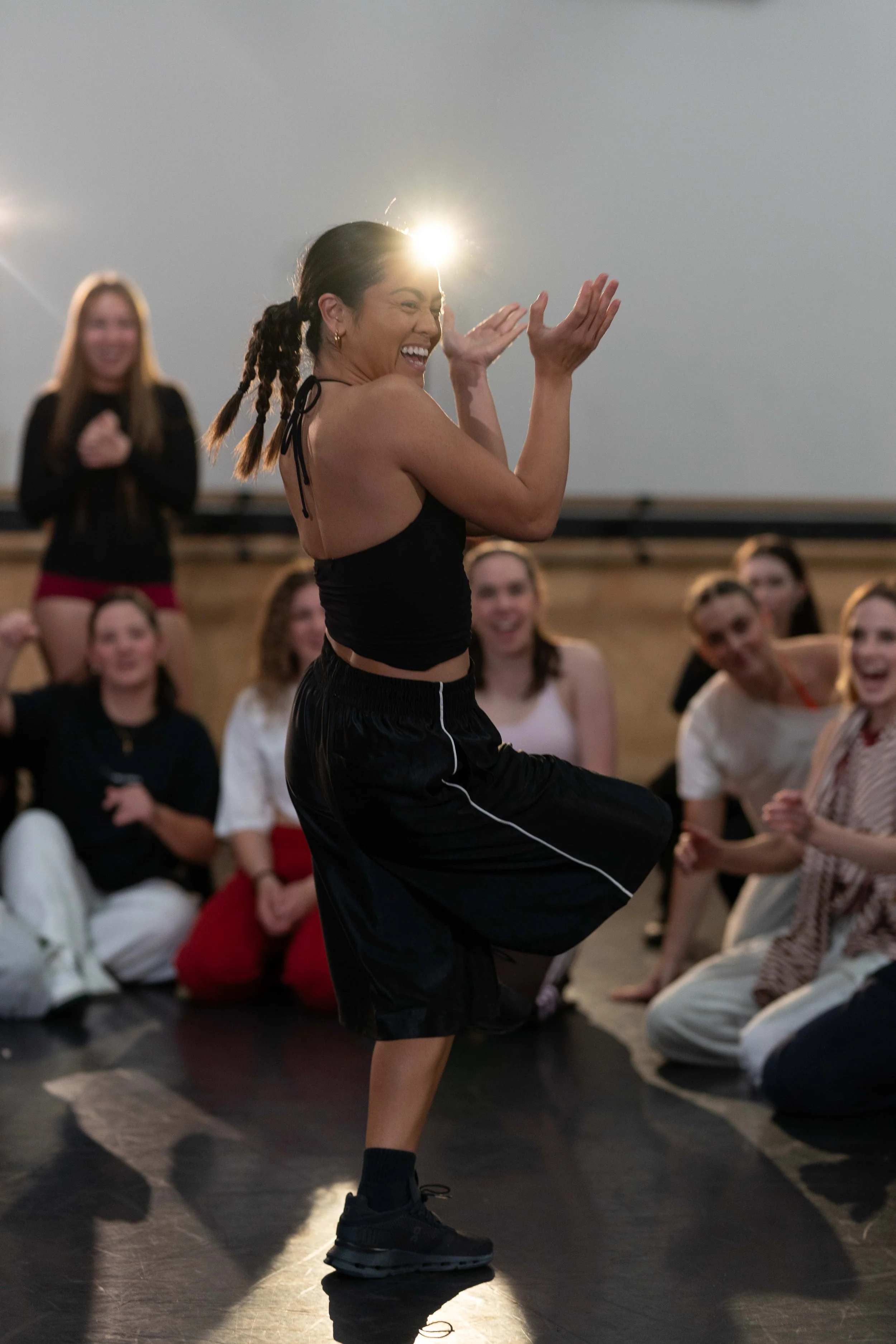 Woman dancing joyfully in front of a group of people indoors.