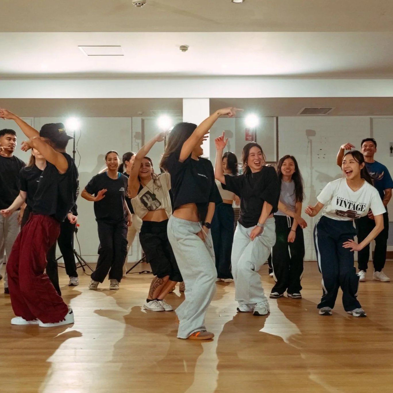 Group of young people dancing and having fun in a dance studio with wooden floors and bright lighting.