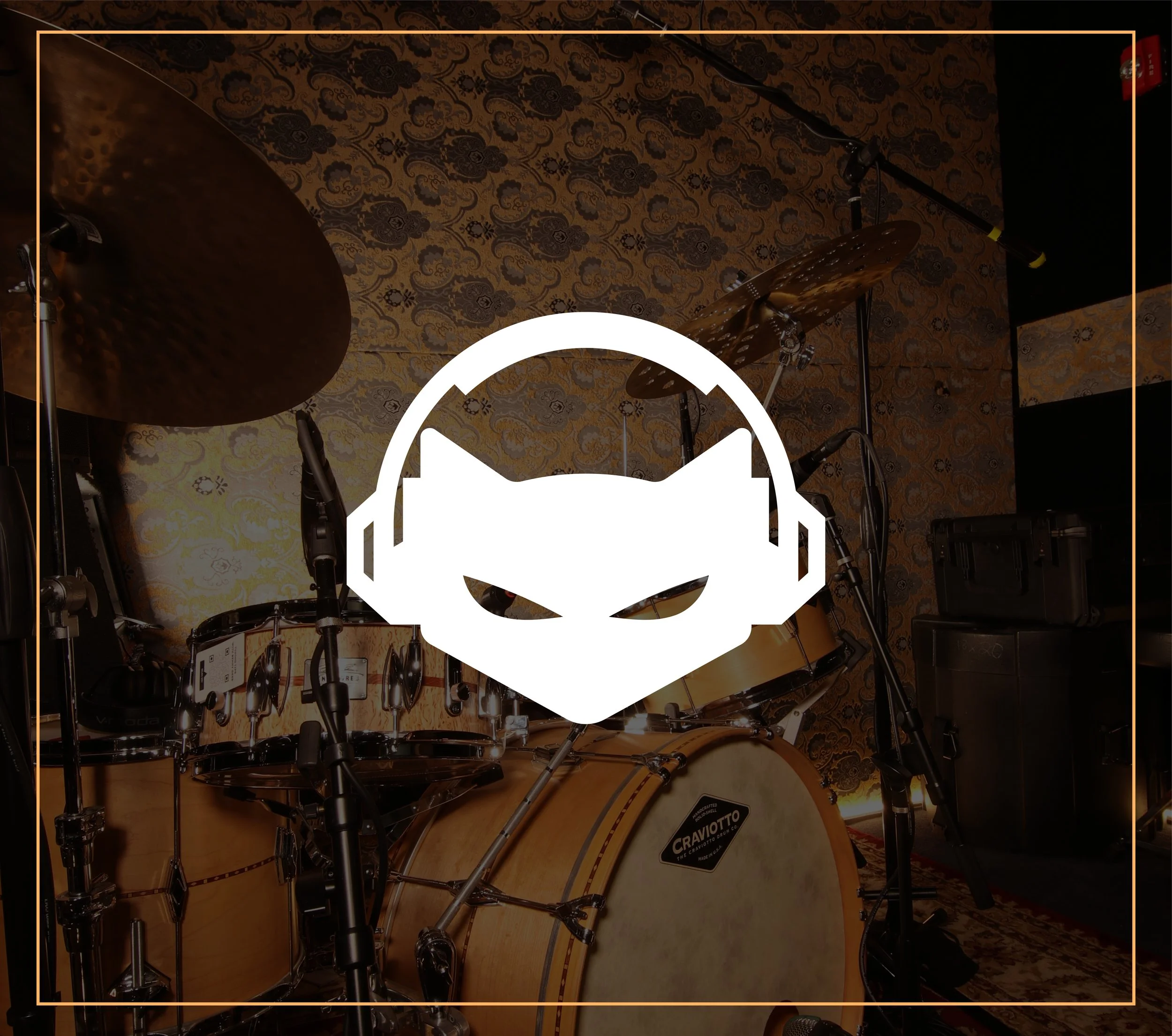 Photo of a drum set with a patterned brown and gold wallpaper in the background and sound equipment visible.