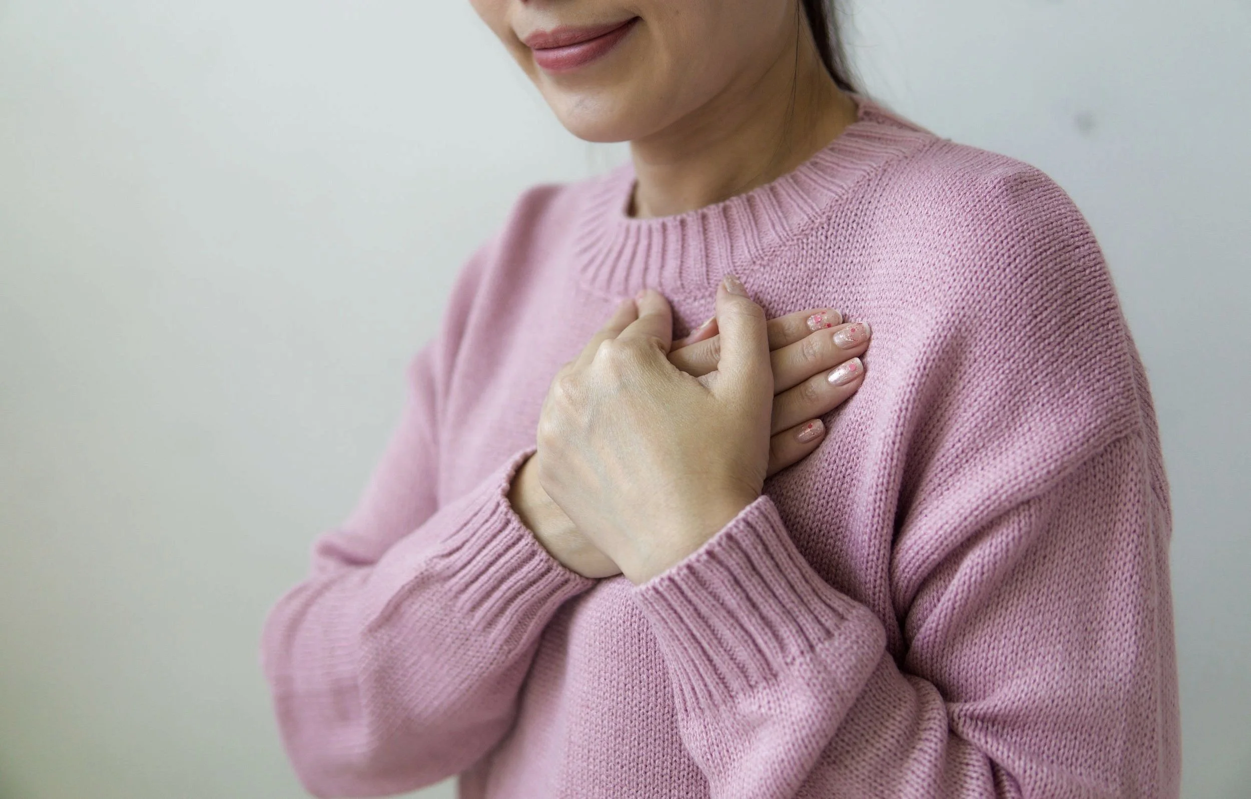 A woman in a pink sweater holding her hand over her heart.