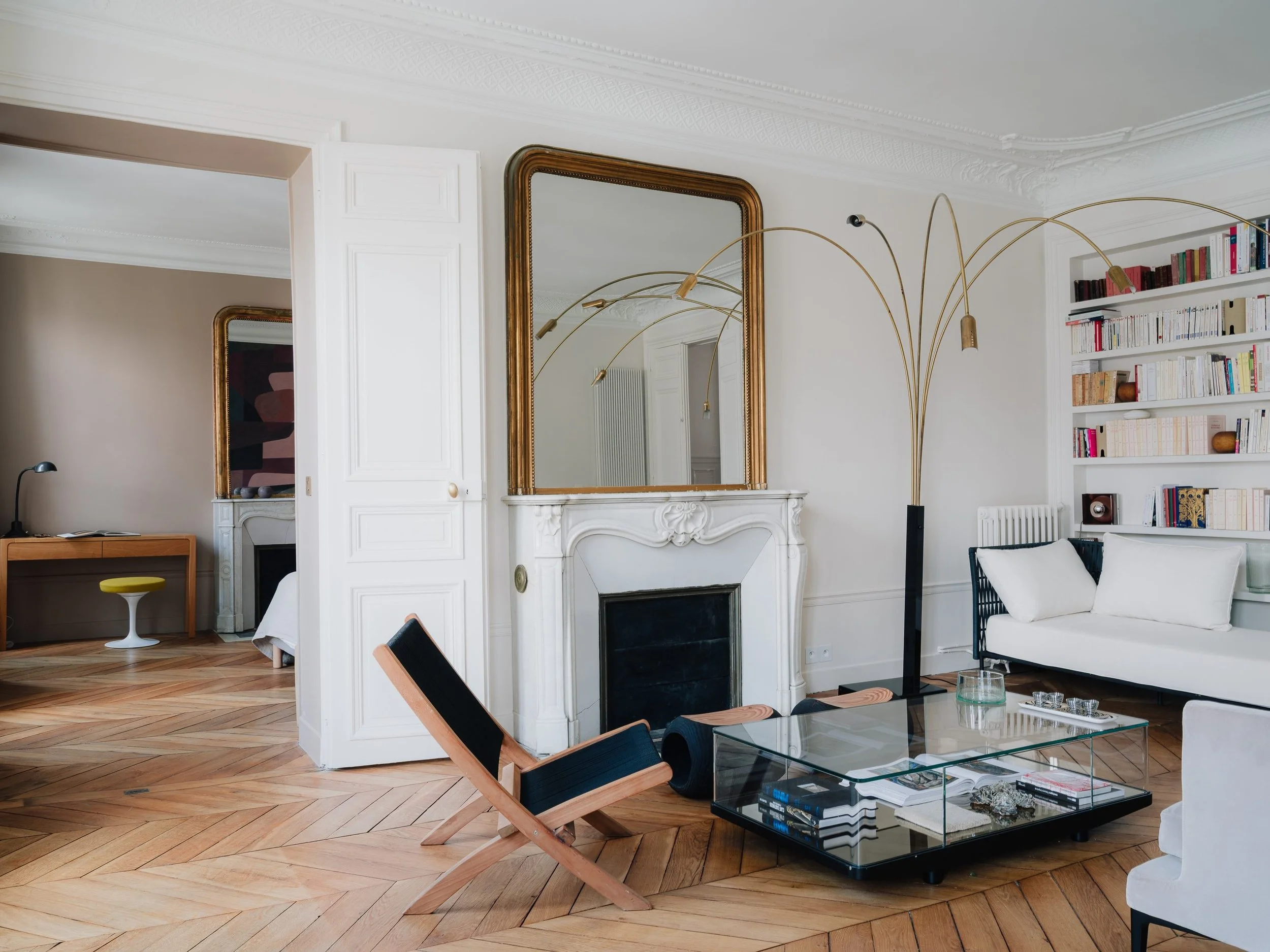 Salon intérieur élégant avec cheminée en marbremiroirs doré, sofa blanc, étagère de livres,  table basse en verre, lampadaire en métal.