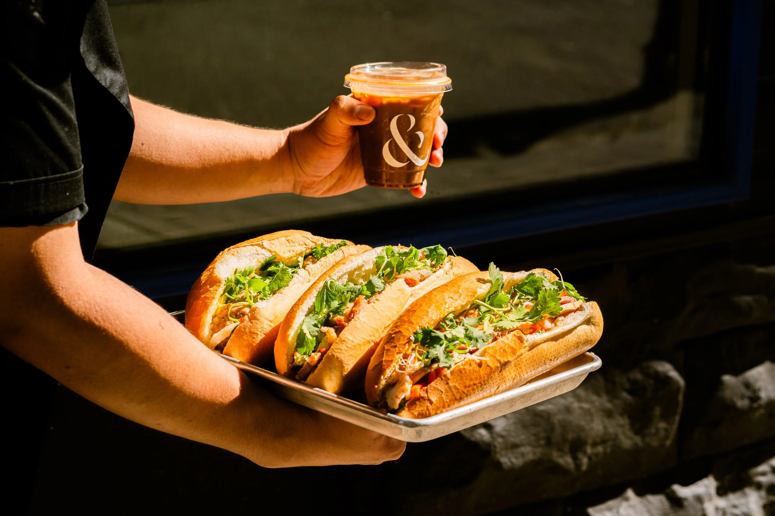 Person holding a tray with sandwiches and a cup of iced coffee.