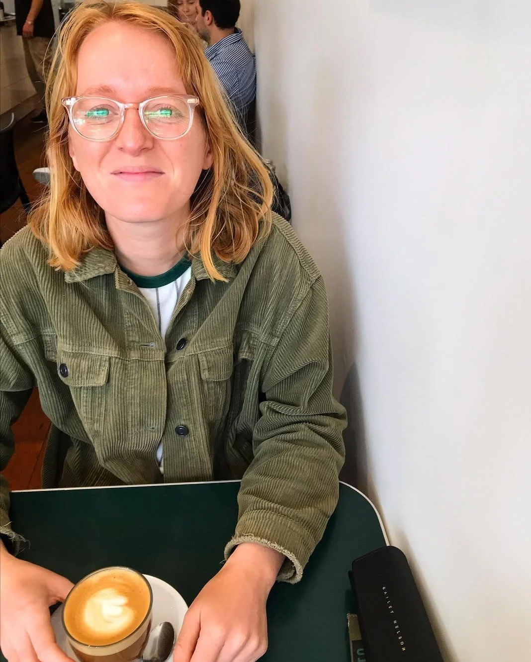Woman sitting in a cafe with a coffee in a green jacket.