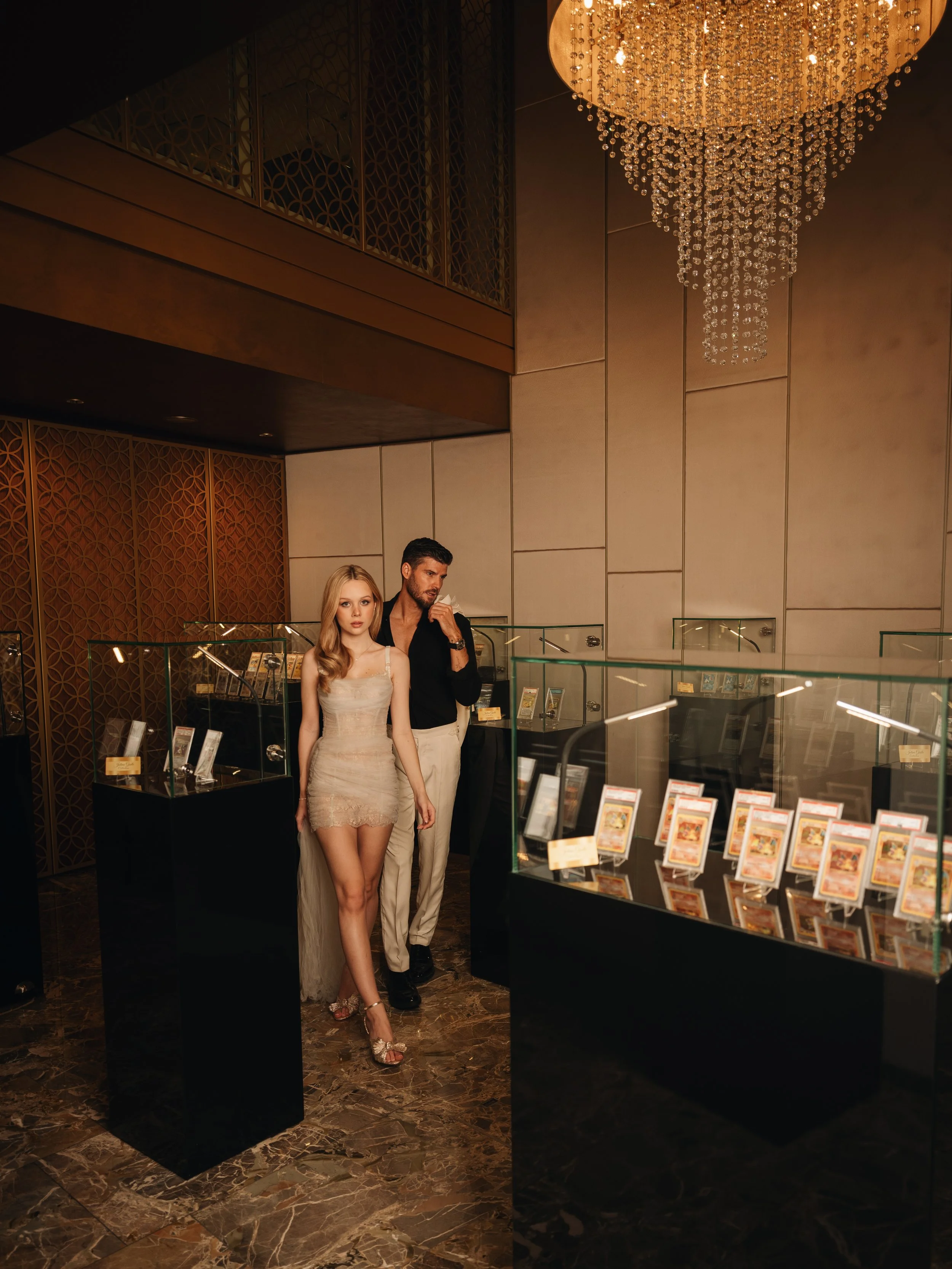 A man and woman exploring a display of collectible cards in a luxurious, well-lit museum or gallery.