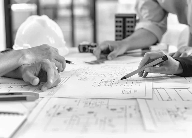 Architects reviewing blueprints and architectural plans on a desk with a hard hat in the background.