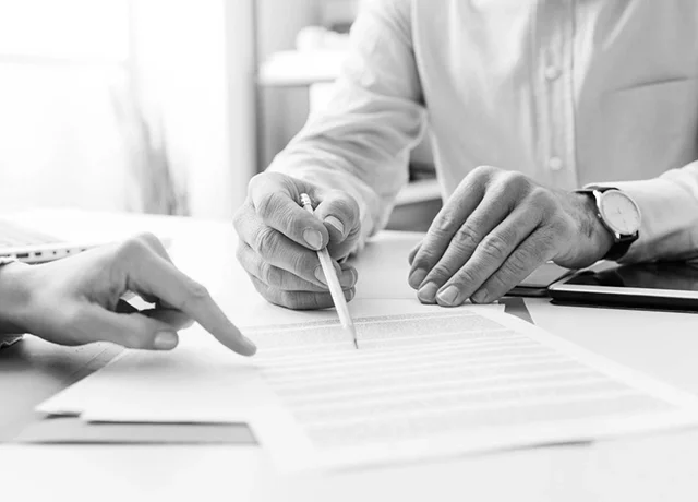 Two people reviewing documents at a desk, one with a pen pointing at the paper.