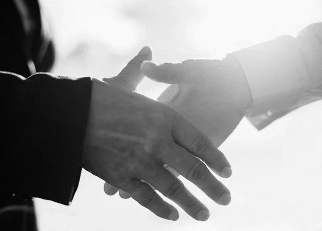Two people shaking hands, with one in a dark suit and the other in a light suit, in a black and white photo.