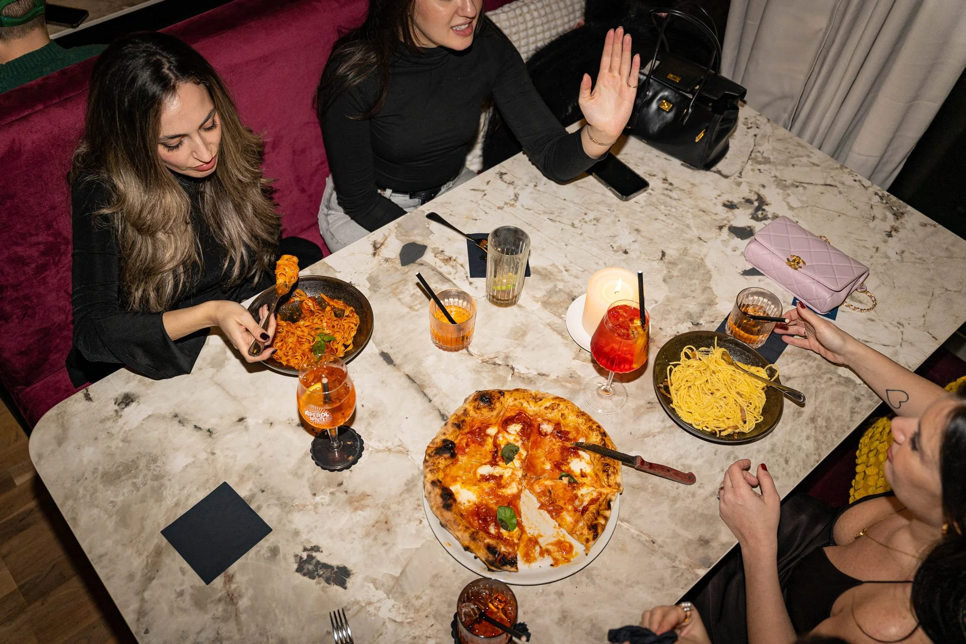 Menschen, die an einem Esstisch Pizza, Pasta und Cocktails in einer gehobenen Umgebung essen.