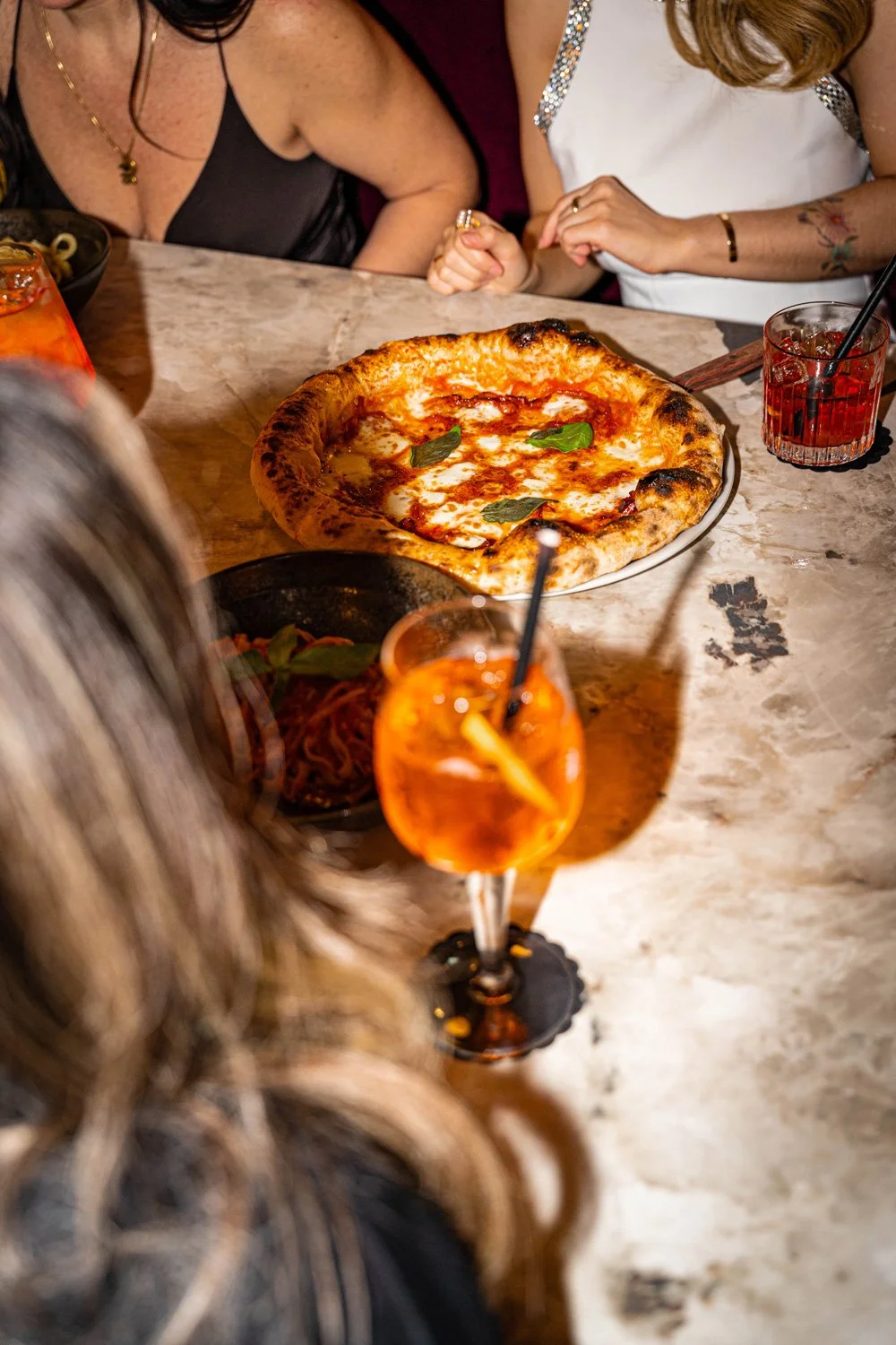 Menschen sitzen um einen Tisch mit Pizza Margherita und Getränken in einem Restaurant.