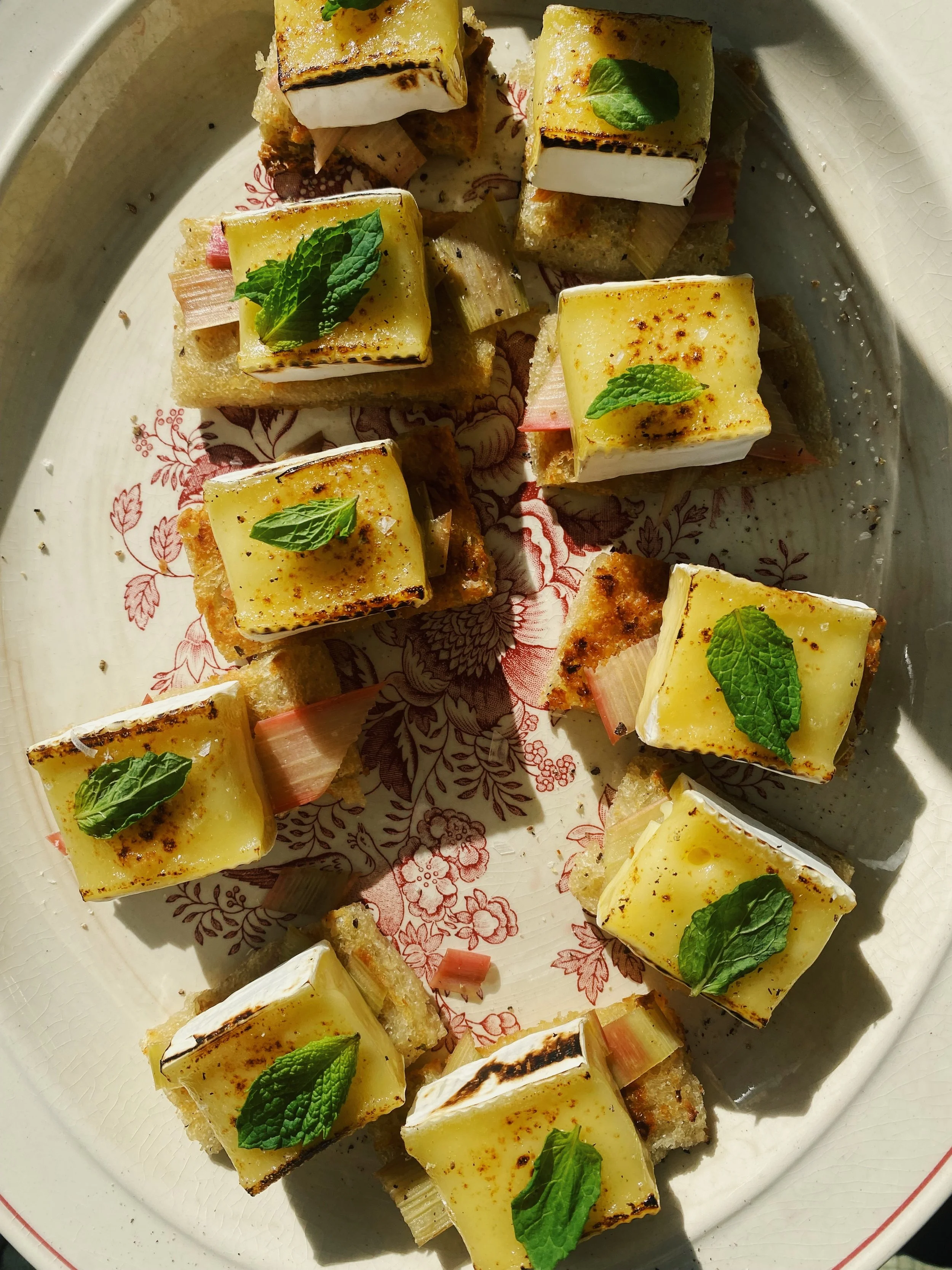 Appetizer with small baked cheese squares garnished with mint leaves, served on toast with onions.