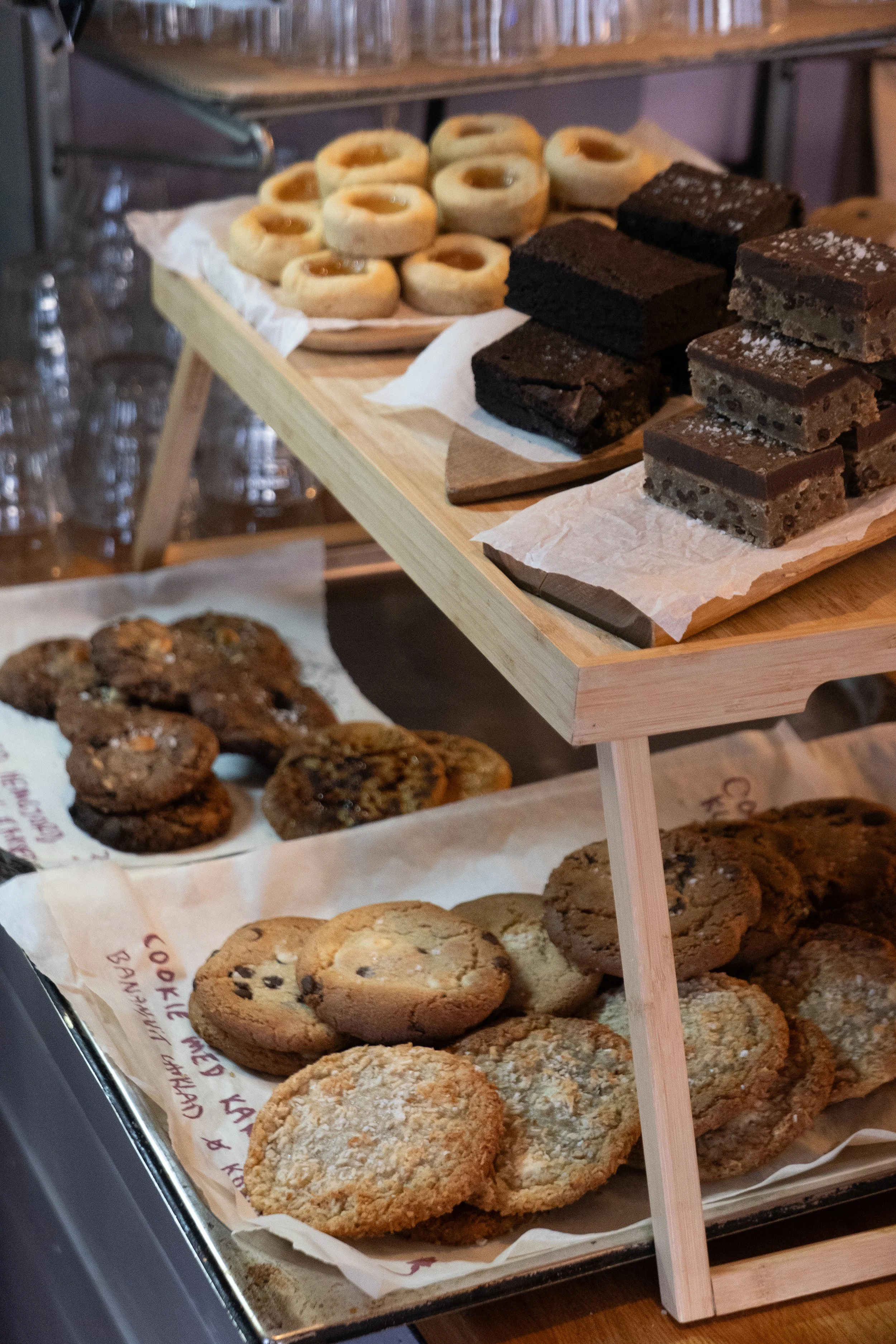 Assorted cookies, brownies, and thumbprint cookies displayed on a two-tier wooden dessert stand and a tray.