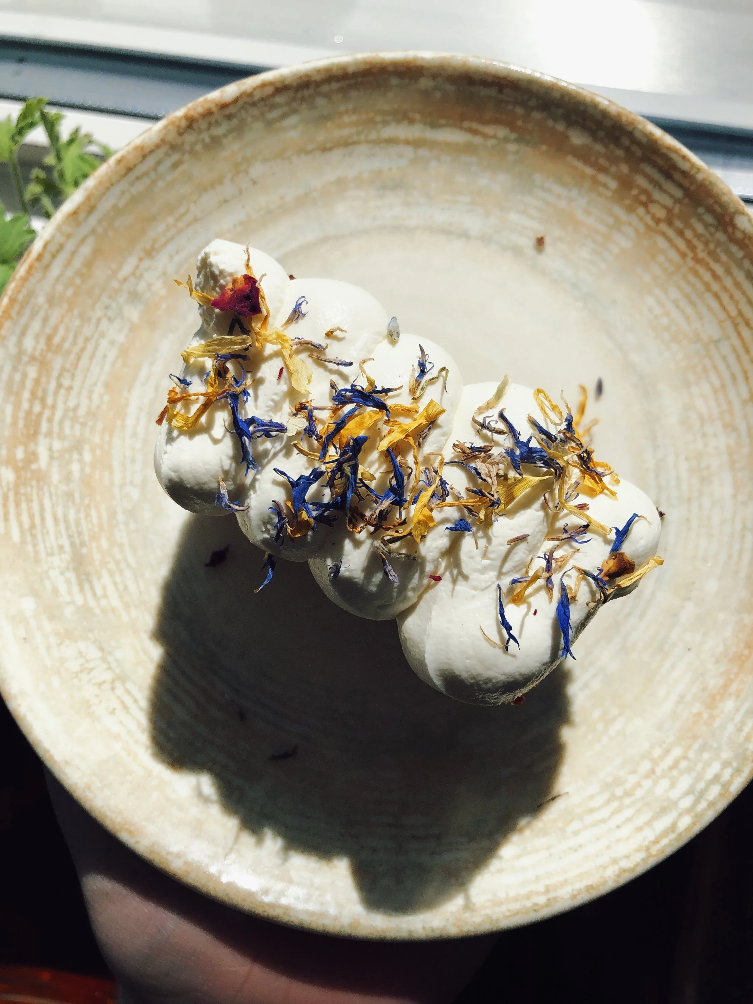 A dessert with a dollop of whipped cream topped with blue and yellow edible flowers, served in a ceramic bowl.